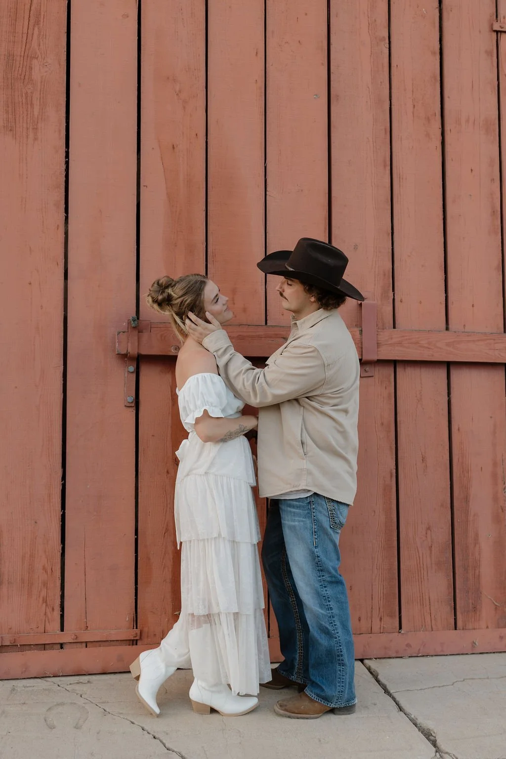 Couple leaning against a red barn door at Los Penasquitos Ranch House