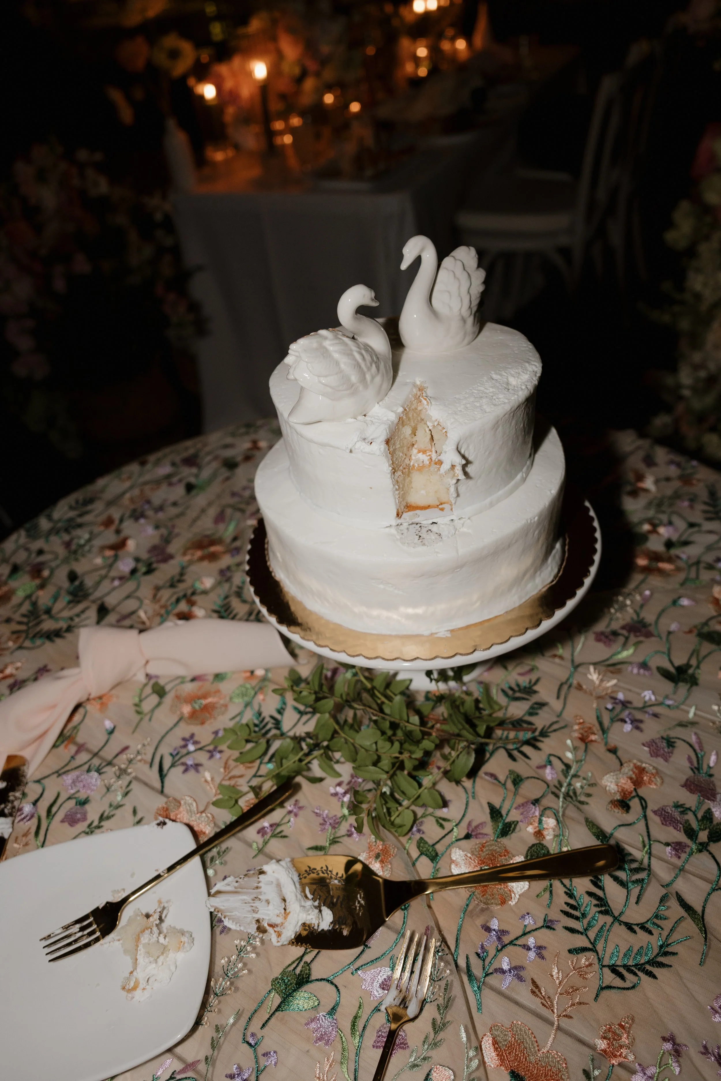 Swan wedding cake after the cutting with gold forks on a floral tablecloth