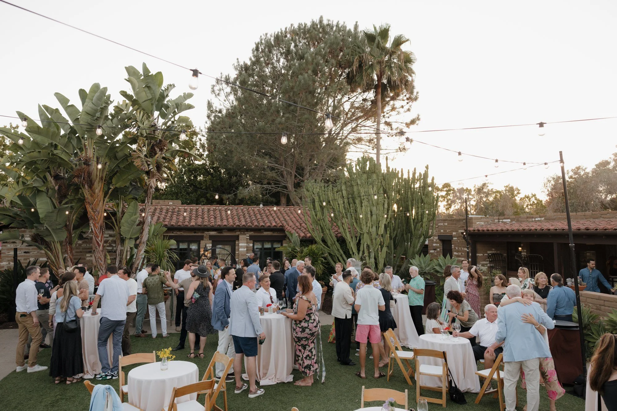 Guests mingling on the garden lawn under string lights at Ryan and Sean's Estancia La Jolla rehearsal dinner