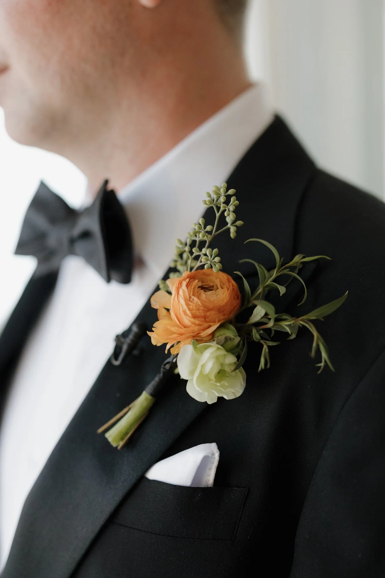 Orange rose and greenery boutonniere pinned to a black tuxedo lapel