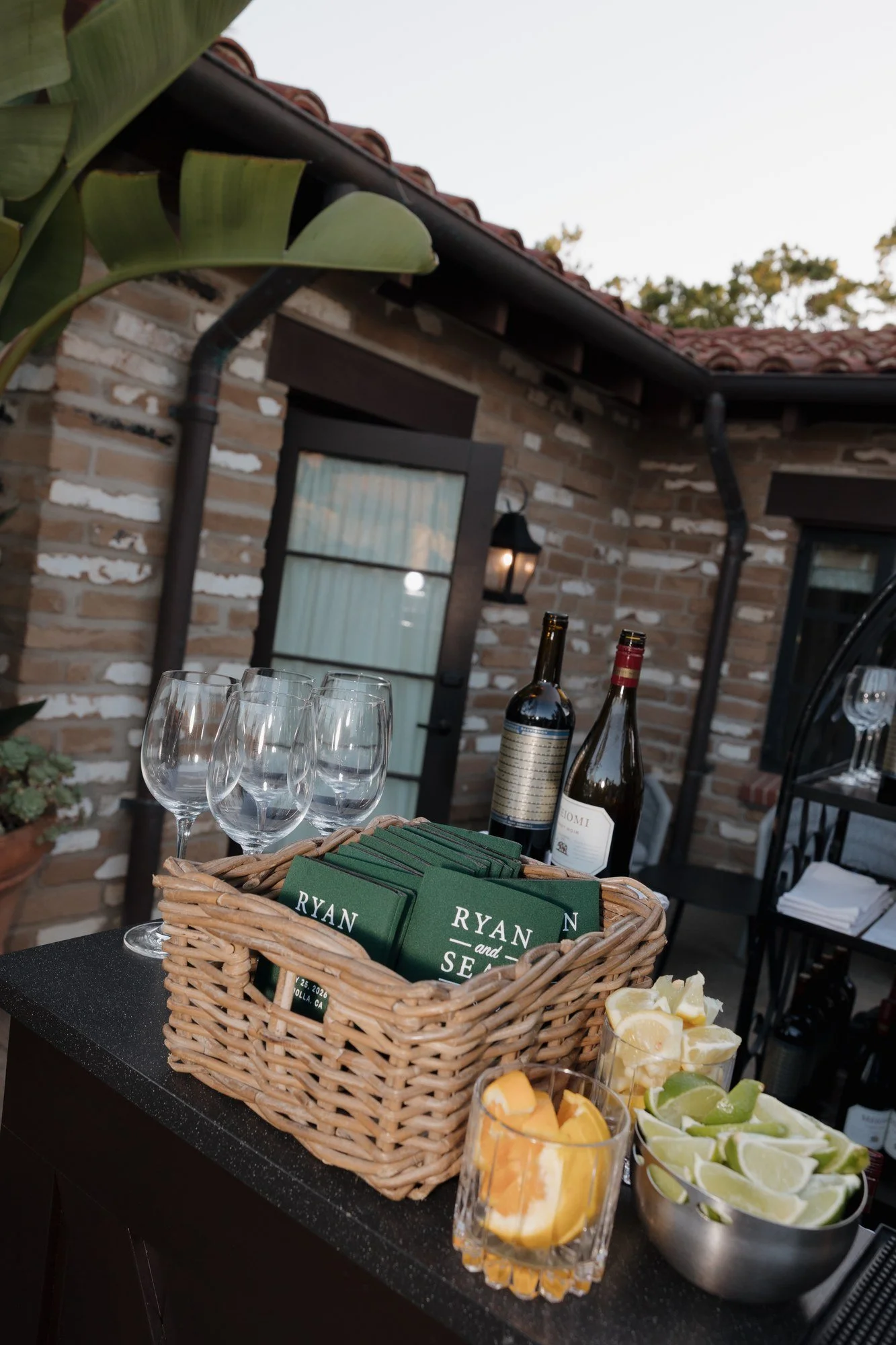Rehearsal dinner bar with wine, glassware and a basket of custom koozies at Estancia La Jolla