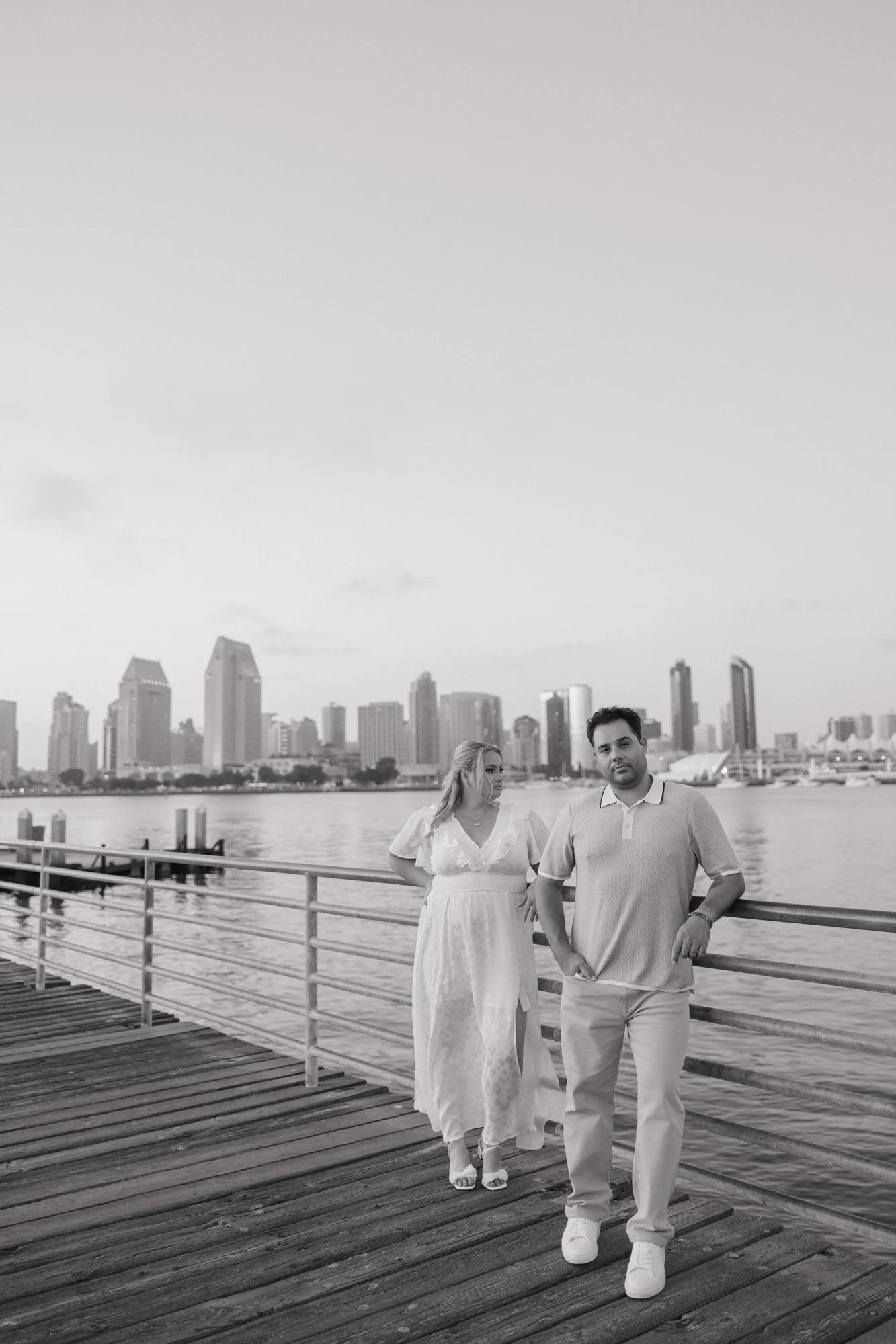Black and white engagement photo of a couple on the Coronado ferry landing pier with the San Diego skyline