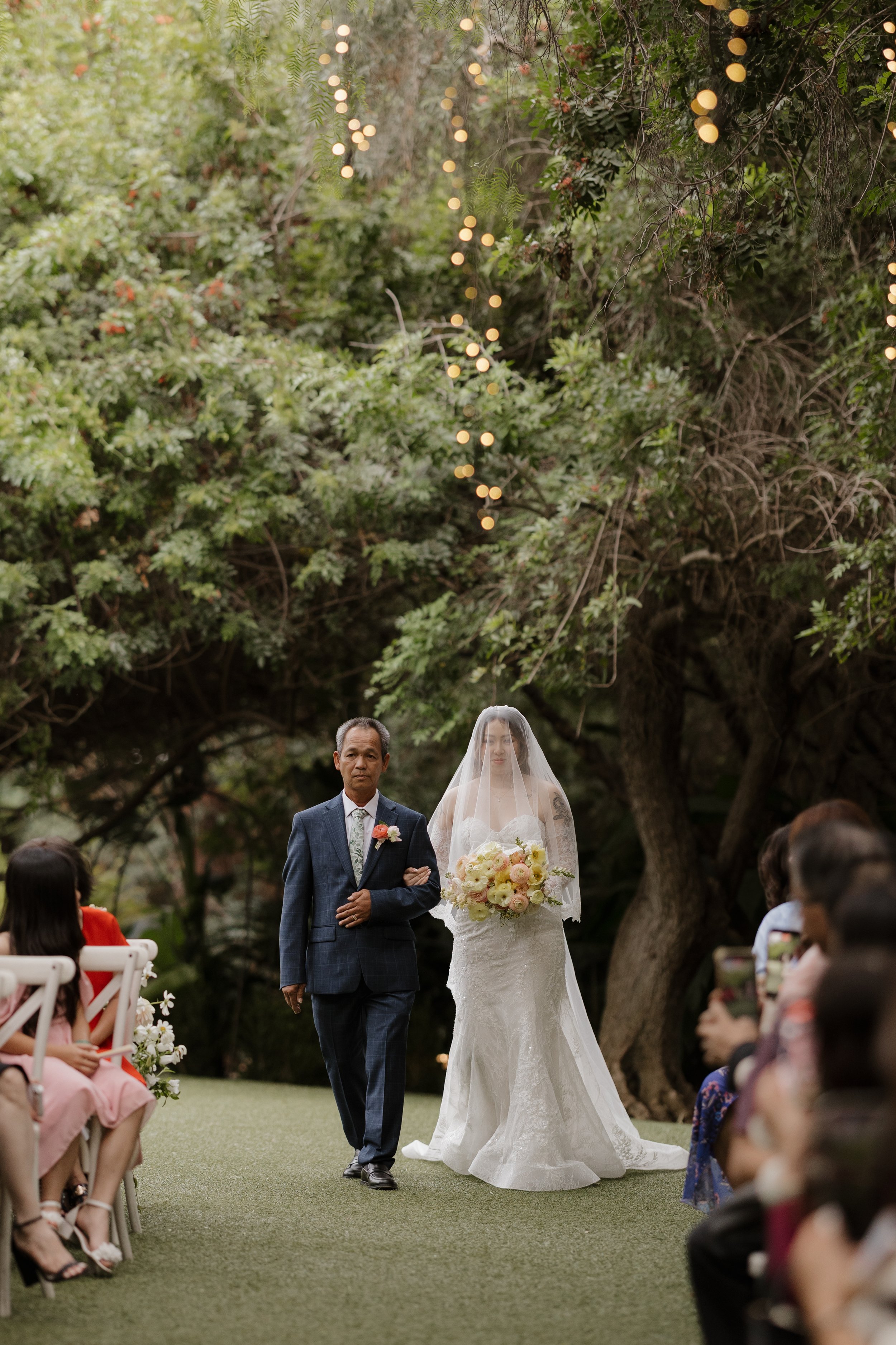 Nancy walking down the aisle under twinkle lights at Green Gables Wedding Estate