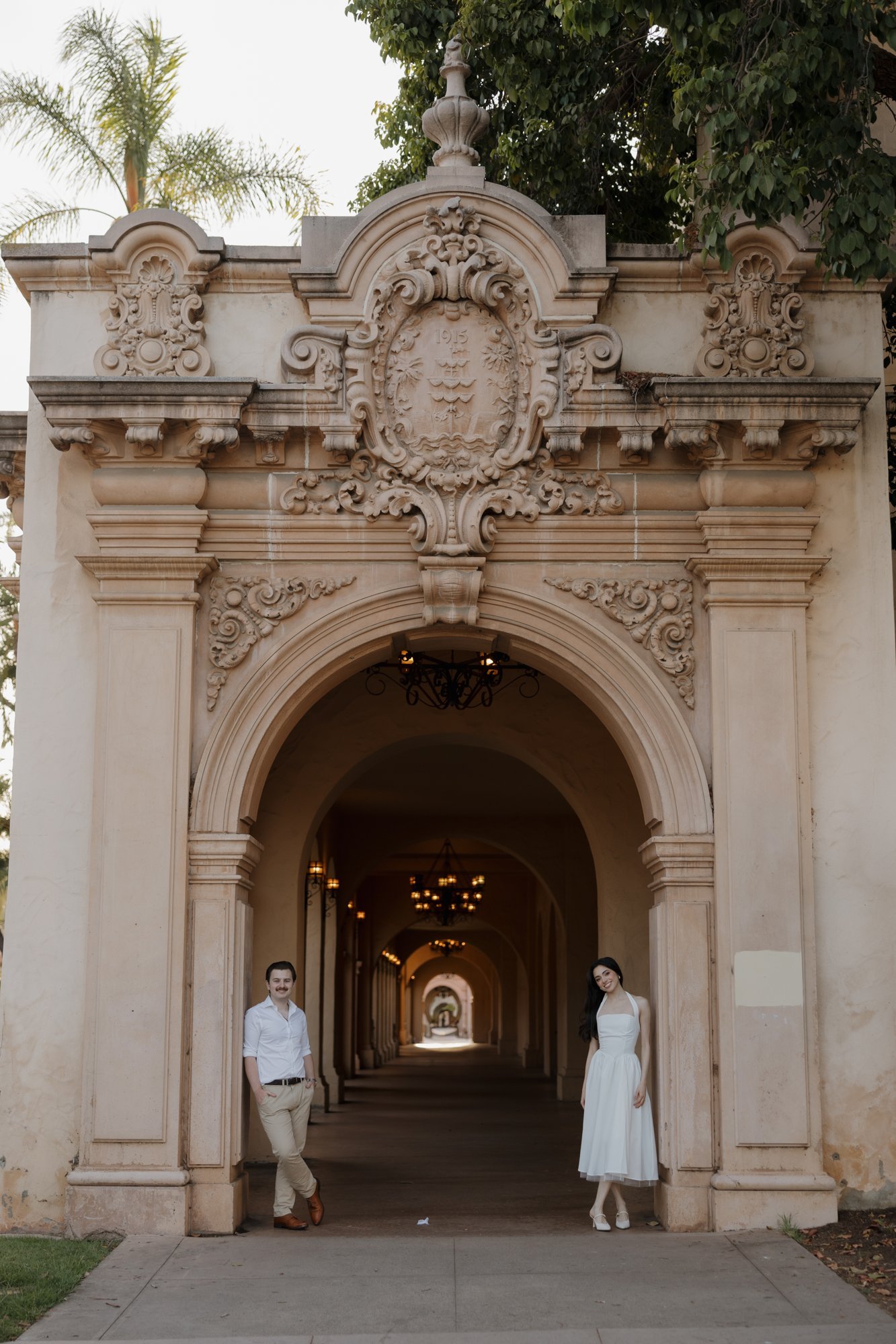 Engaged couple standing under an ornate Spanish Colonial archway in Balboa Park, San Diego