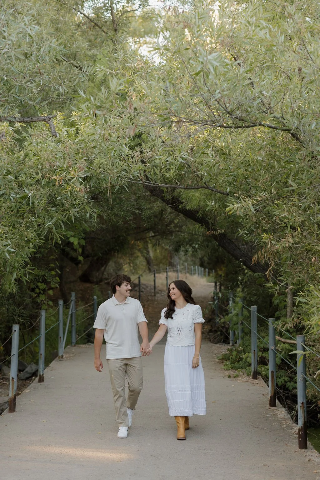 Couple walking hand in hand under a tunnel of trees at Mission Trails Regional Park