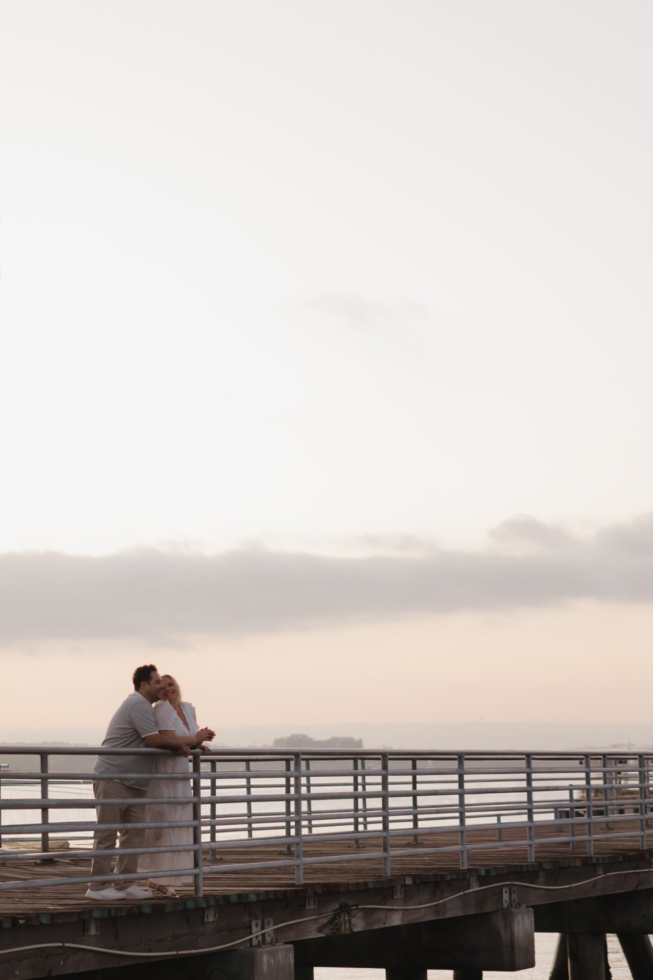 Couple leaning on the pier railing at sunset in Coronado