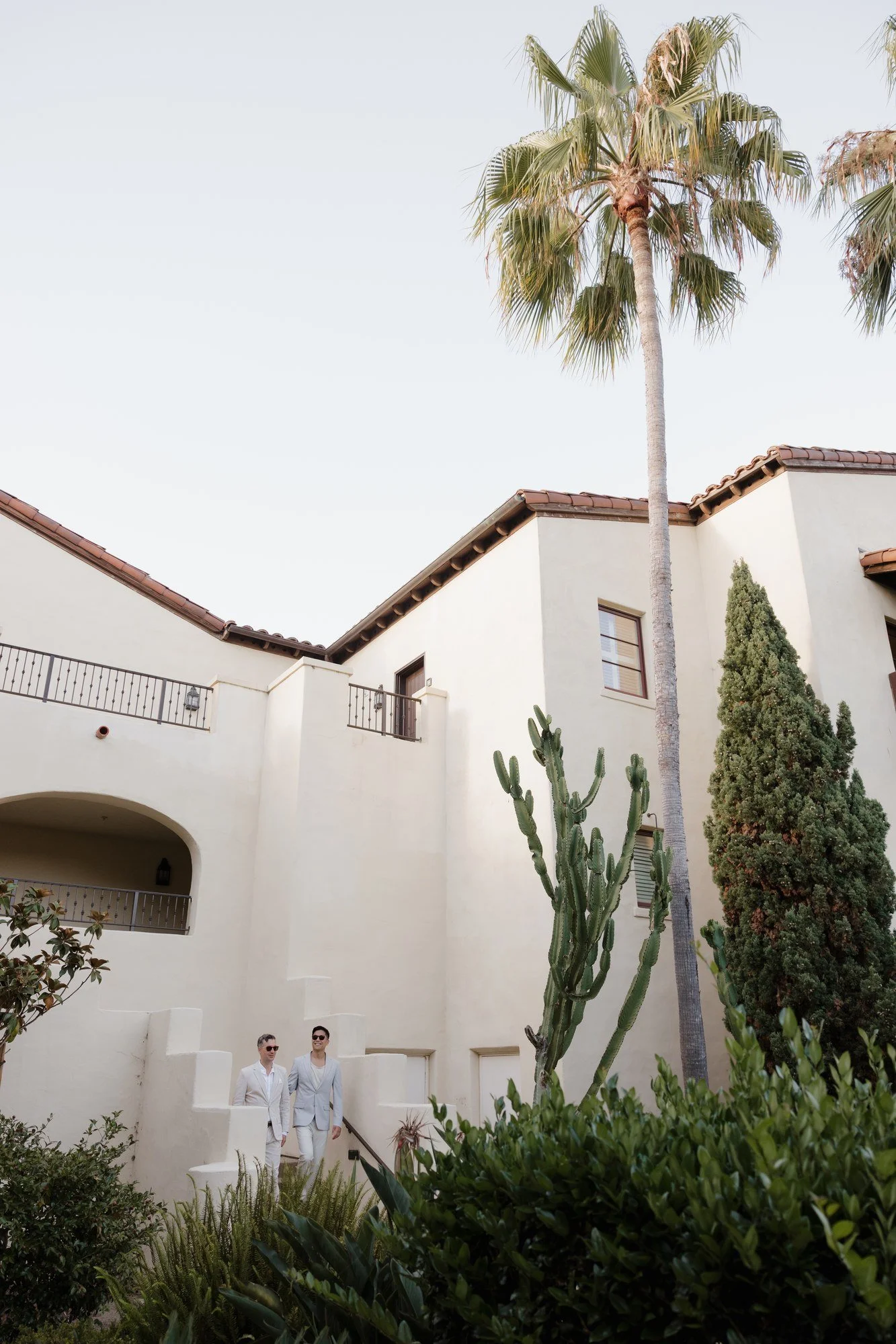 Ryan and Sean small in frame beneath white hacienda walls and palms at Estancia La Jolla
