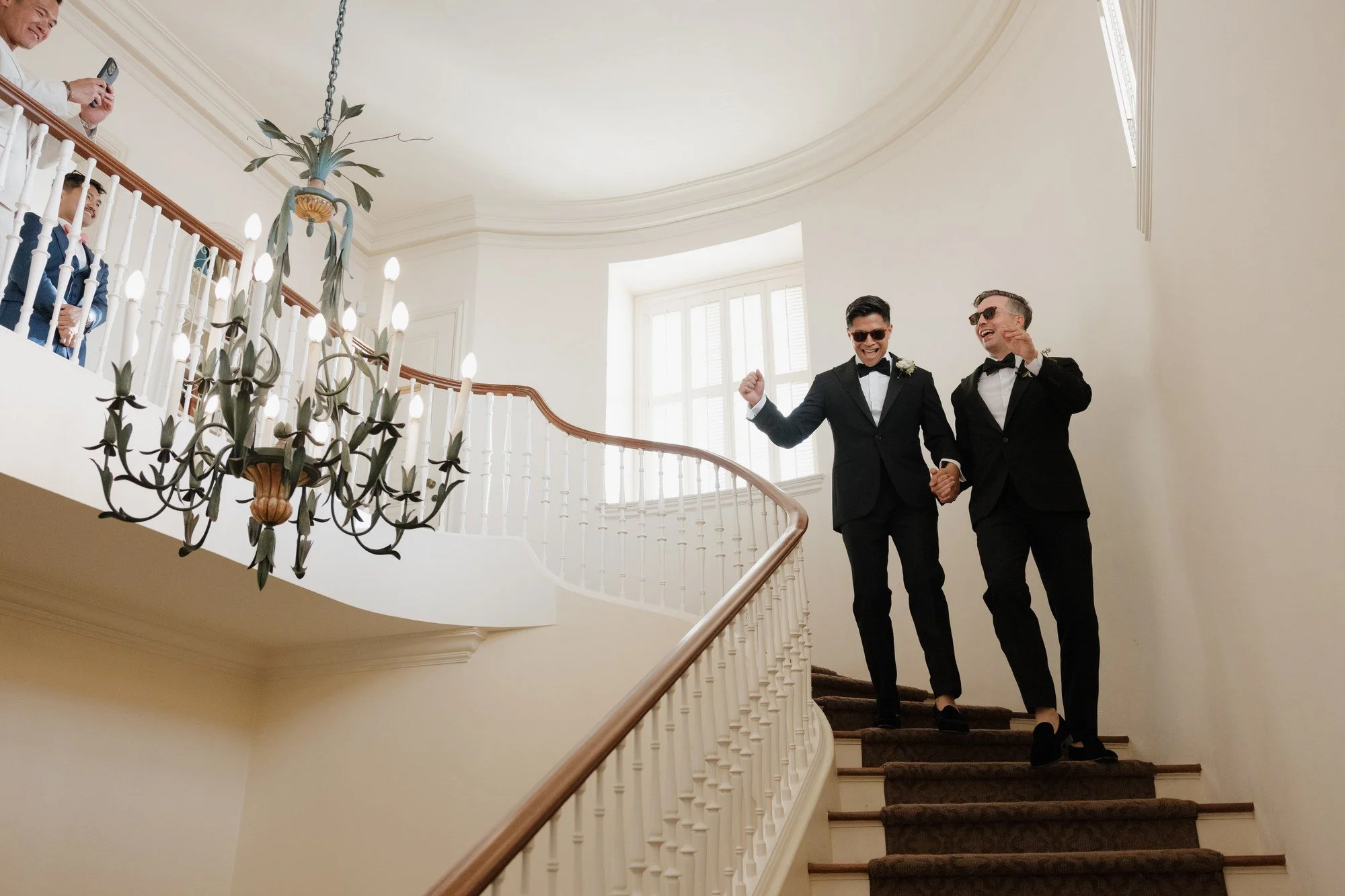 Ryan and Sean walking down the curving grand staircase under the chandelier at Darlington House