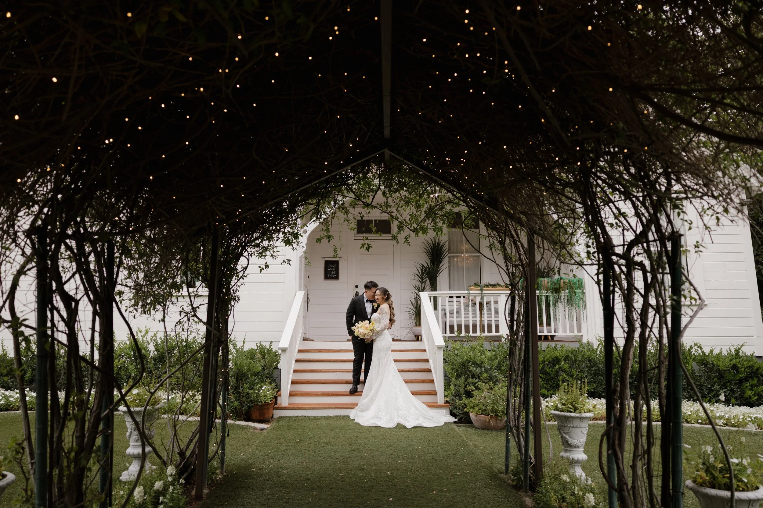 Nancy and Ken framed by a vine-covered arbor in front of the schoolhouse at Green Gables