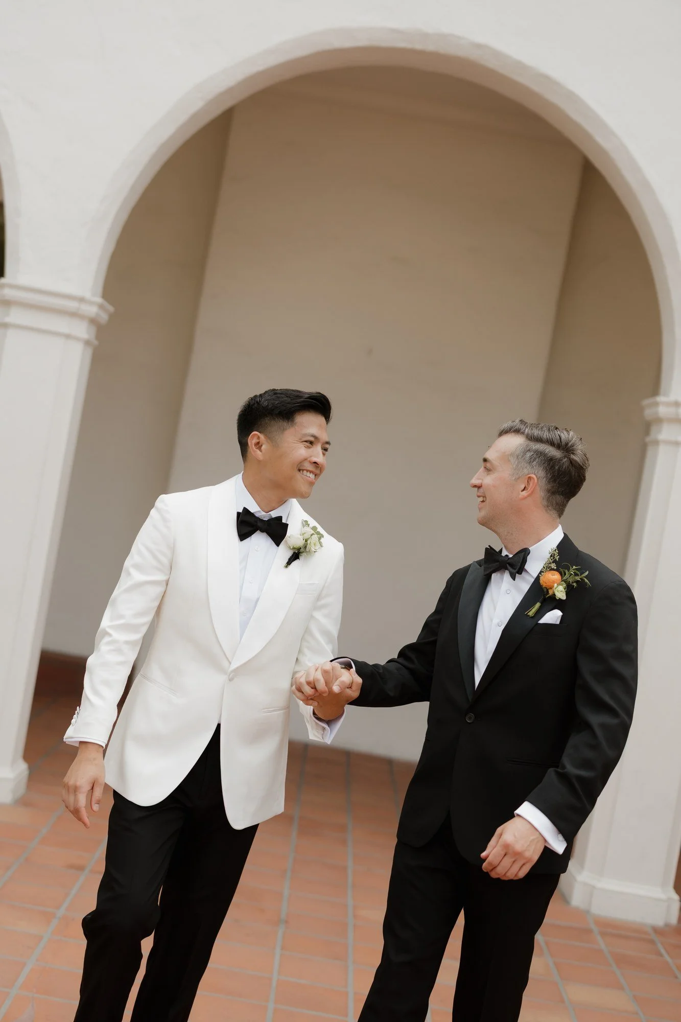 Ryan and Sean smiling and holding hands after their first look under the arches at Darlington House in La Jolla