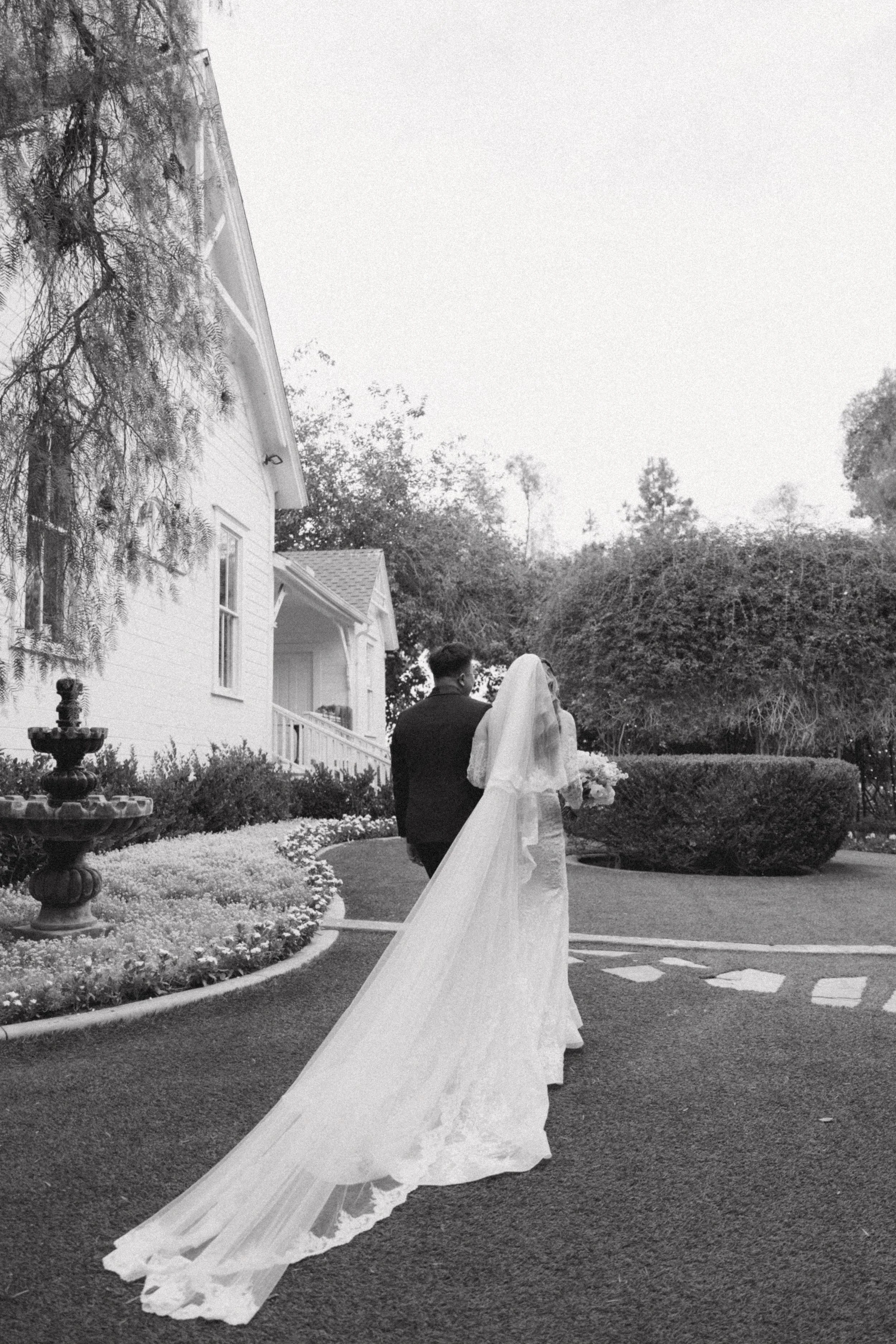 Black and white portrait of Nancy's long veil trailing as she walks with Ken at Green Gables