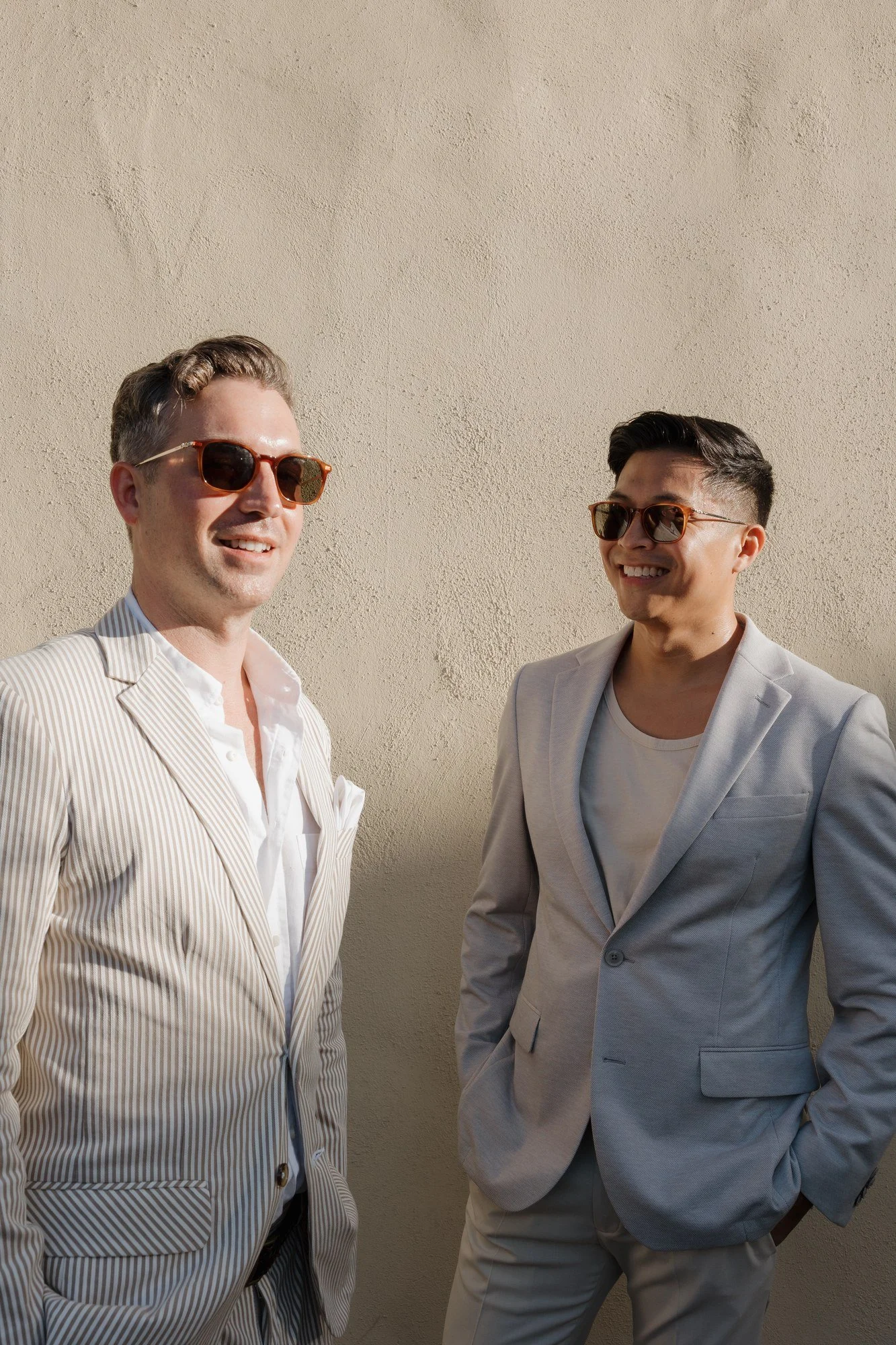 Ryan and Sean laughing in sunglasses against a warm plaster wall at Estancia La Jolla