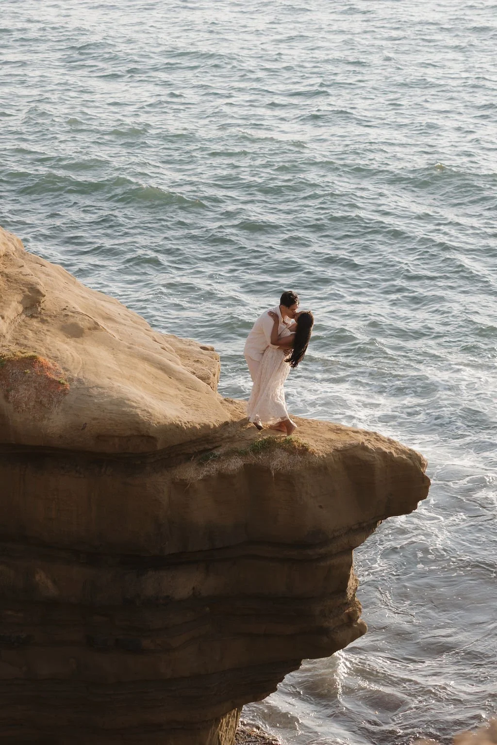 Couple standing on a sandstone arch above the ocean at Sunset Cliffs