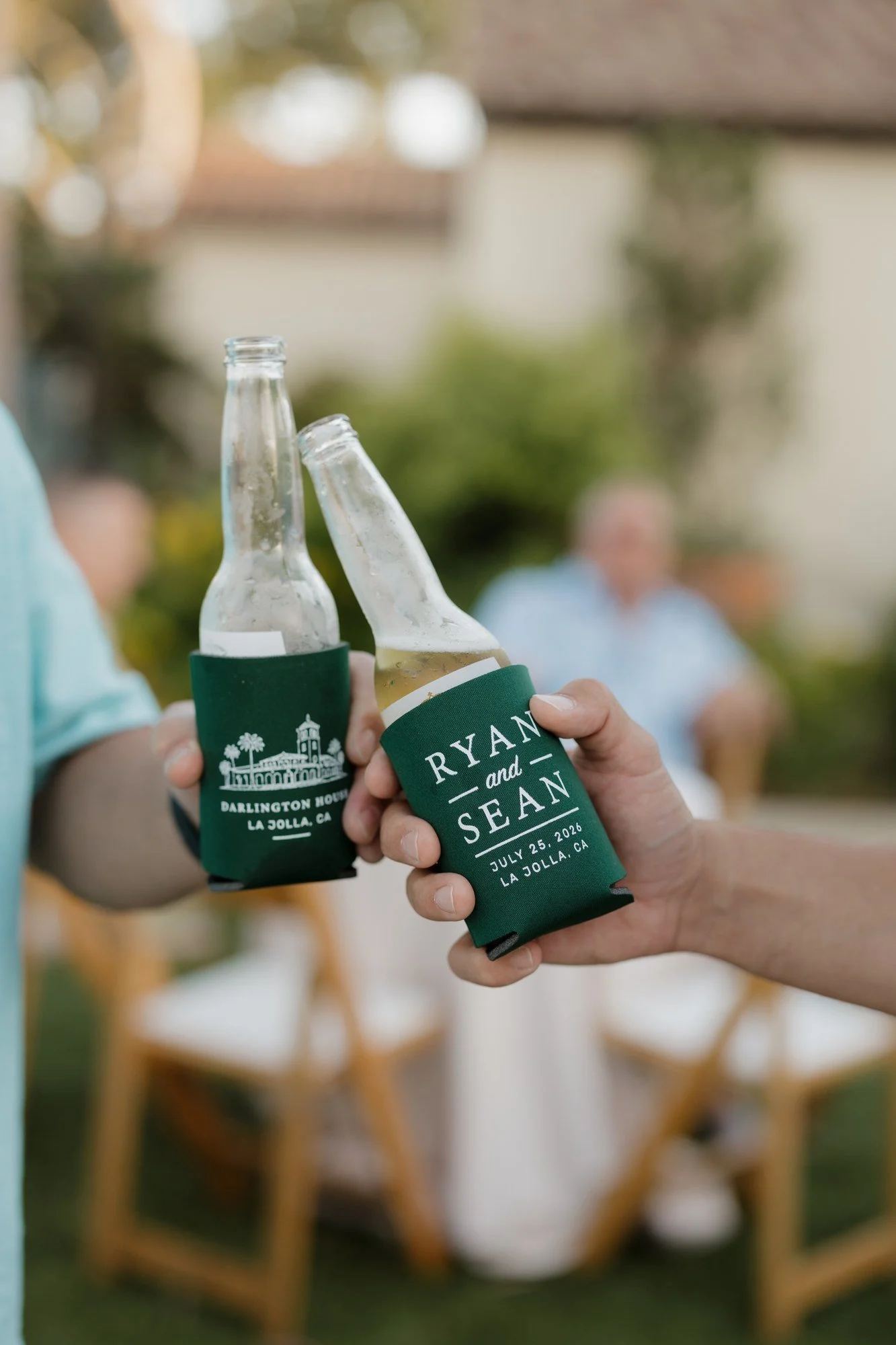 Two guests clinking bottles in custom Ryan and Sean koozies at the rehearsal dinner