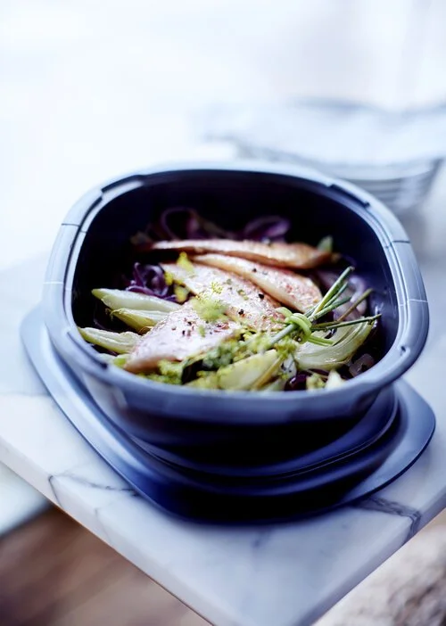 Steamed fish fillets with vegetables in a dark cooking pot on a marble surface.
