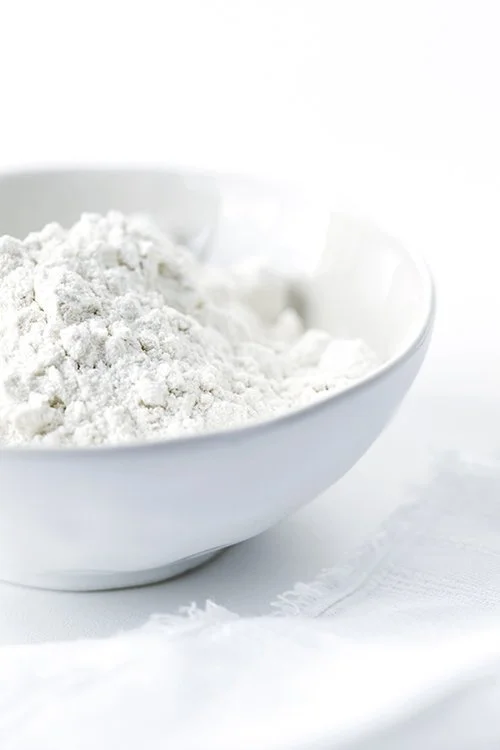 A white bowl filled with white powder on a white surface.