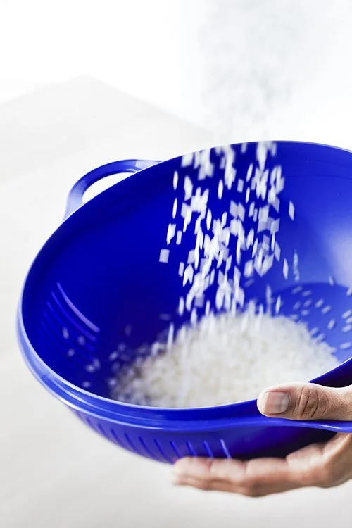 White rice being poured into a blue colander held by a person's hand.