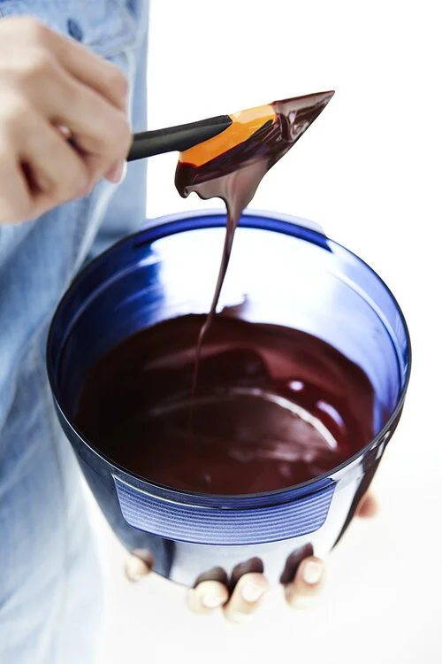 Person holding a blue bowl with melted chocolate being stirred with a spatula.