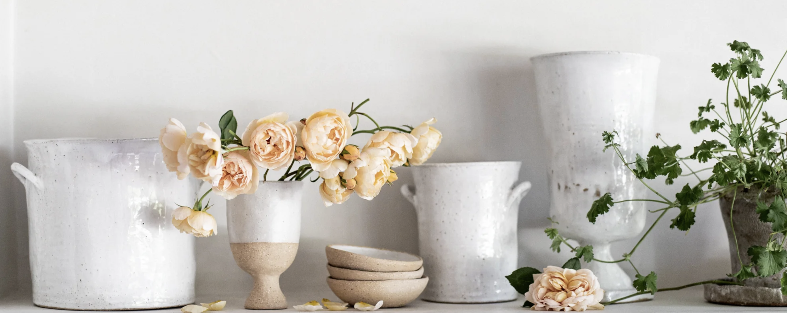 White ceramic vases with textured finish holding peach-colored flowers and greenery on a white shelf.