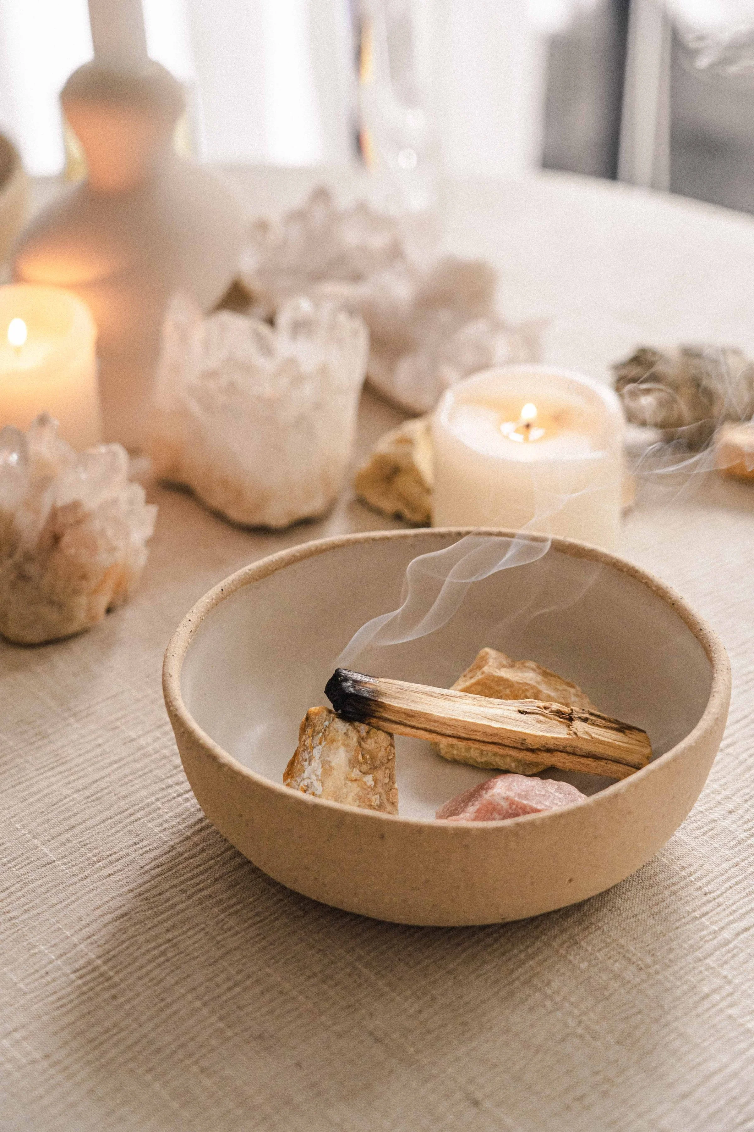 A ceramic bowl with a smoldering stick inside, surrounded by rocks and candles on a table.