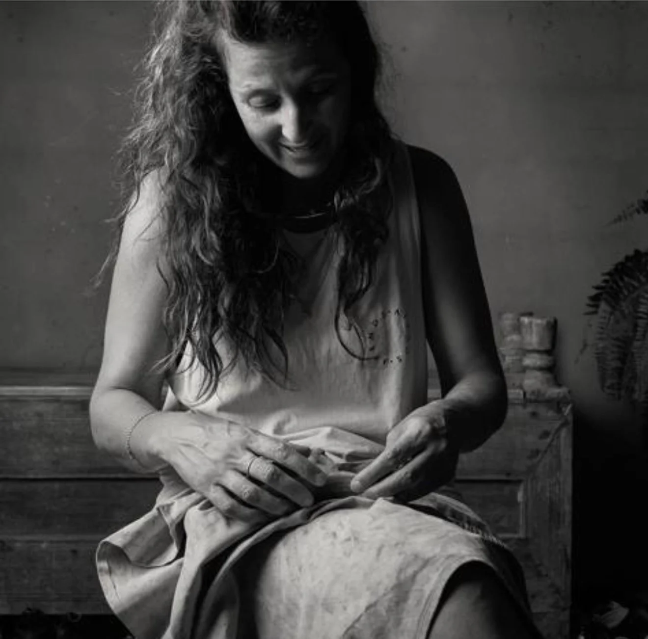 A woman with long, curly hair working on a sculpture in a studio, appearing focused.