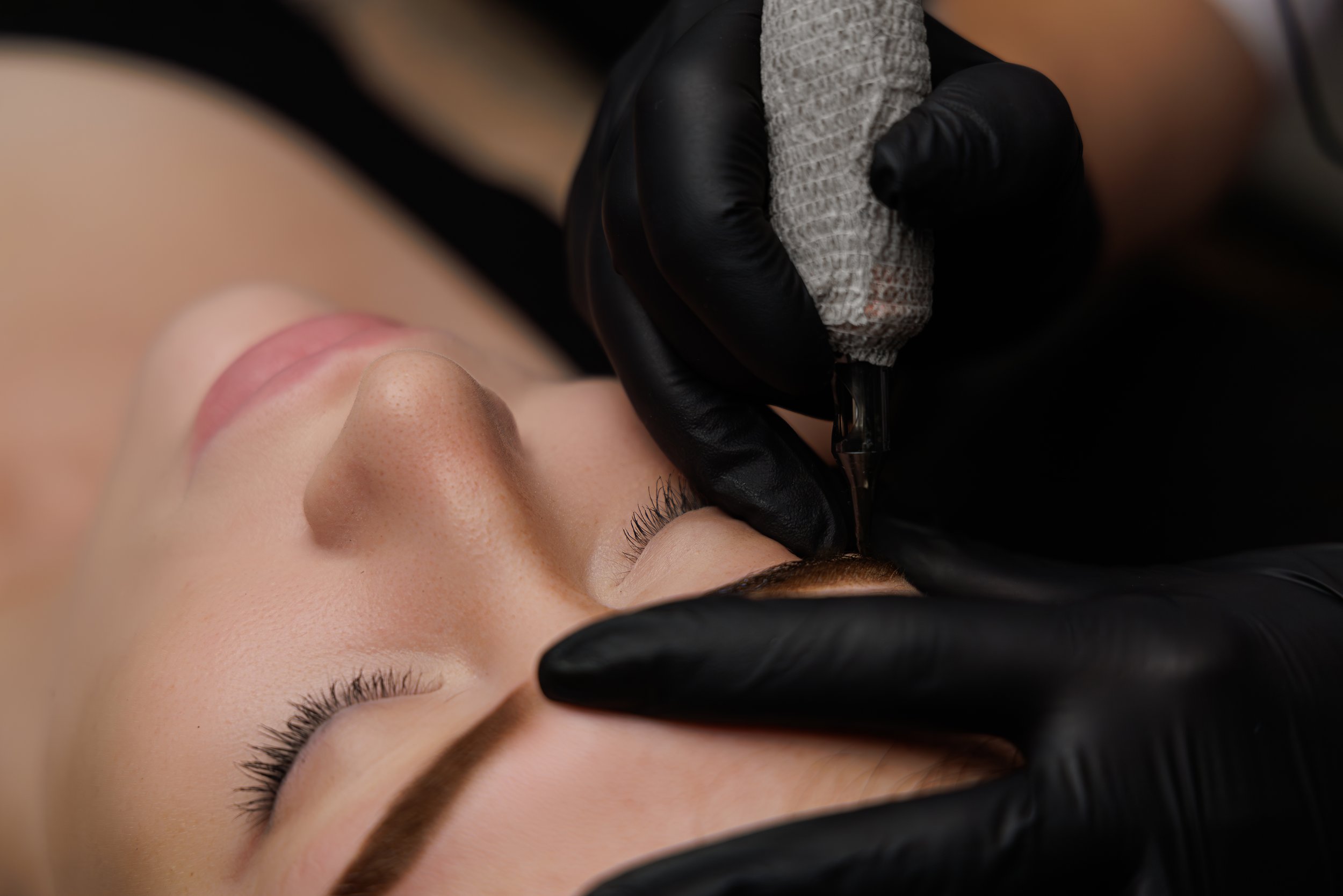 Permanent makeup artist applying eyeliner tattoo during a cosmetic tattoo procedure at Salvation Beauty Ink