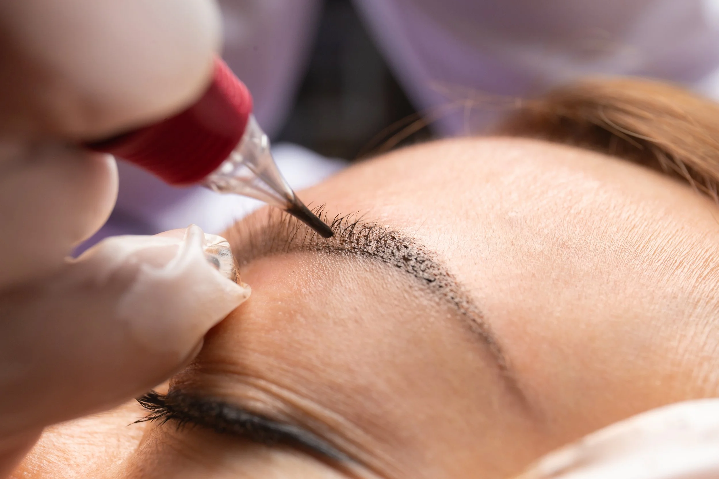 Cosmetic tattoo artist performing eyebrow shading during a permanent makeup session