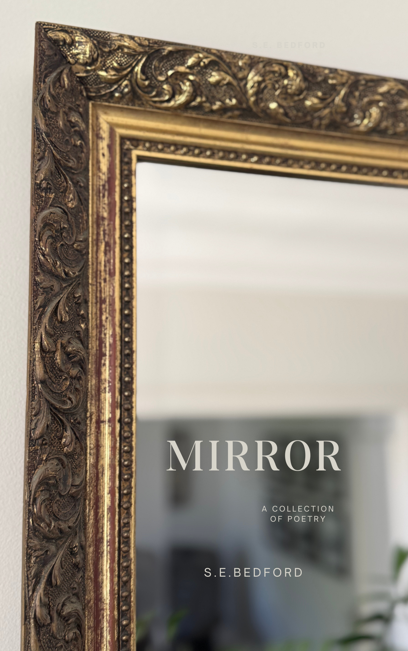 Close-up of an ornate, gold-colored decorative mirror frame with a book titled 'Mirror: A Collection of Poetry' by S. E. Bedford reflected in it.