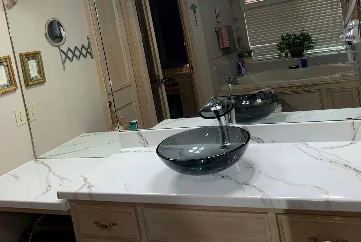 A bathroom vanity with an beautiful epoxy marble countertop and a black oval vessel sink with a tall faucet. A large mirror spans the wall above the vanity.