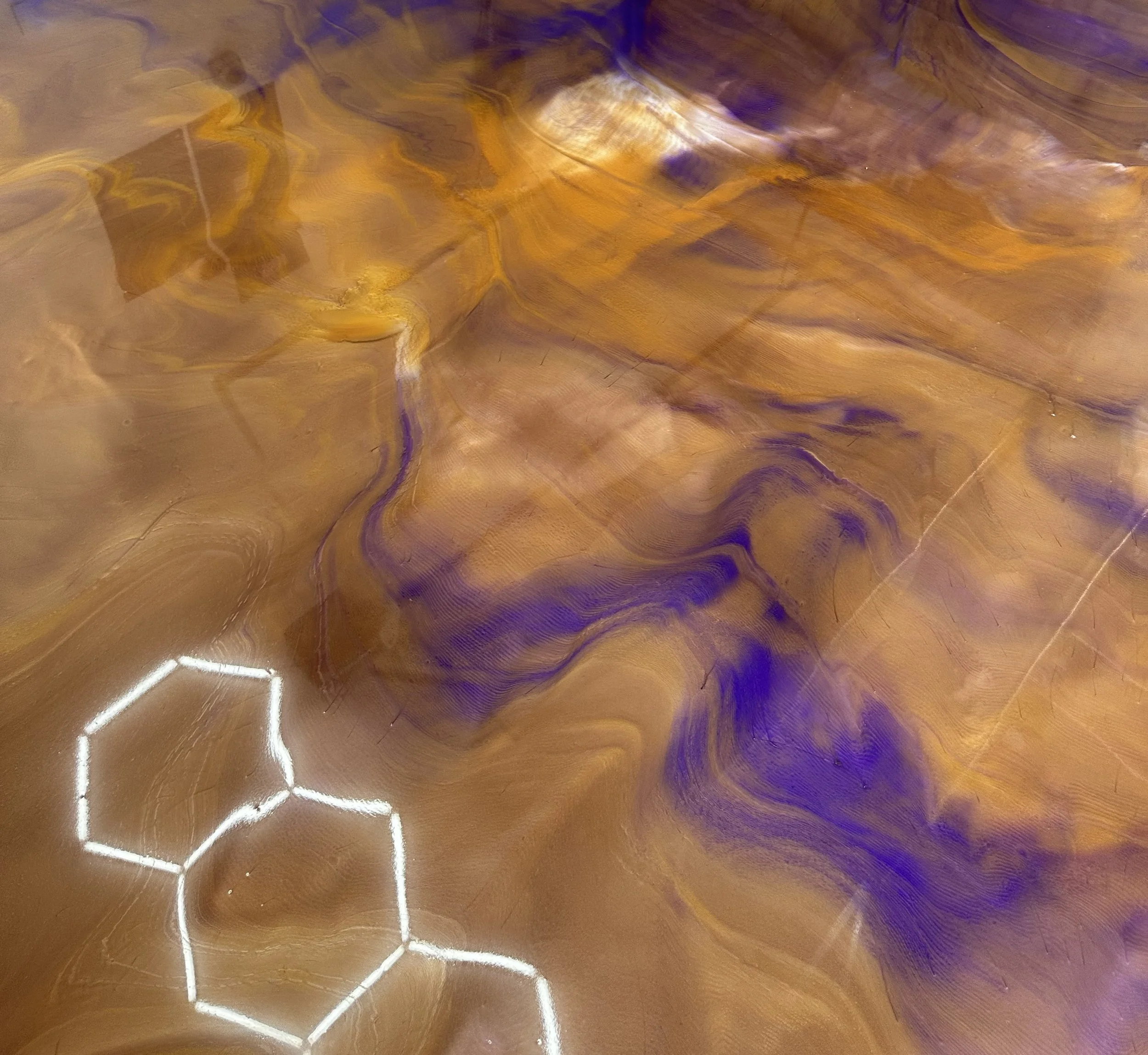 Close-up of a polished epoxy surface with a warm gold tone and intricate purple swirling patterns, reflecting light.