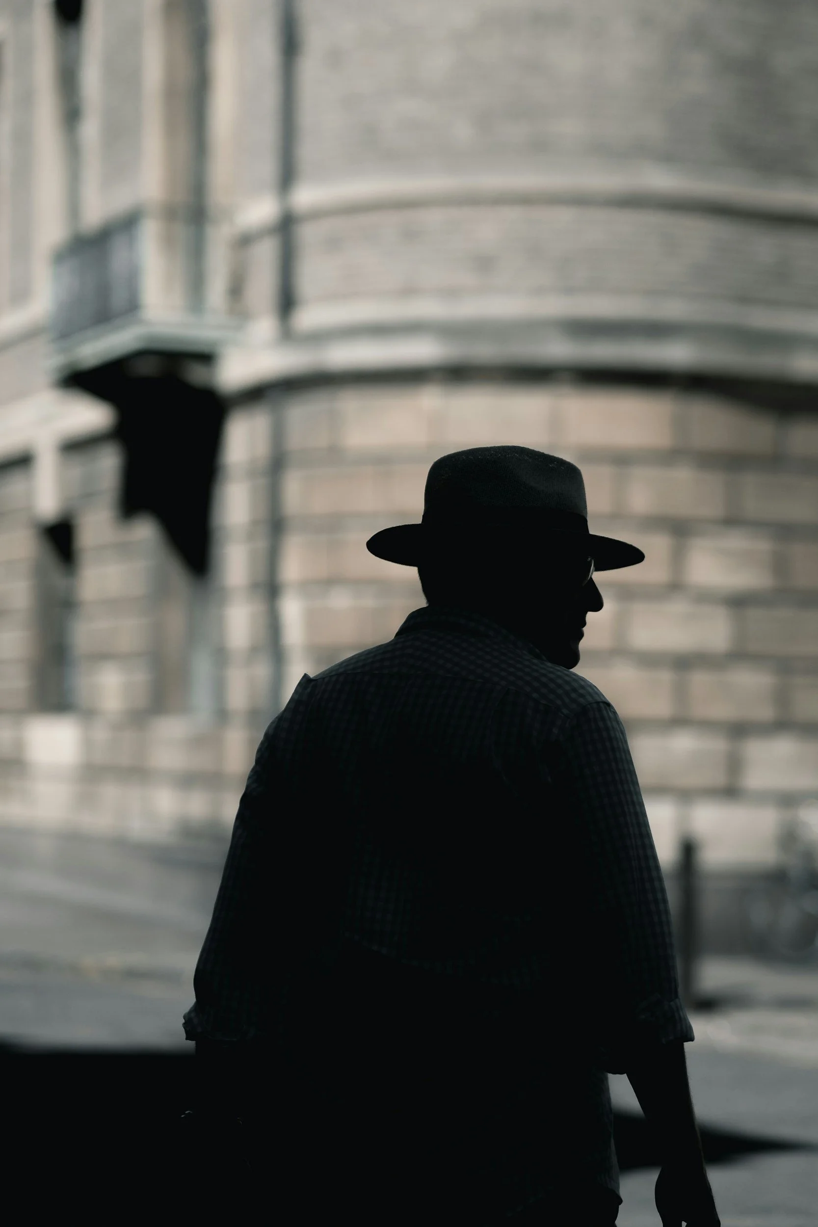 Silhouette of a man wearing a hat and glasses, standing in front of a cityscape with buildings in the background.