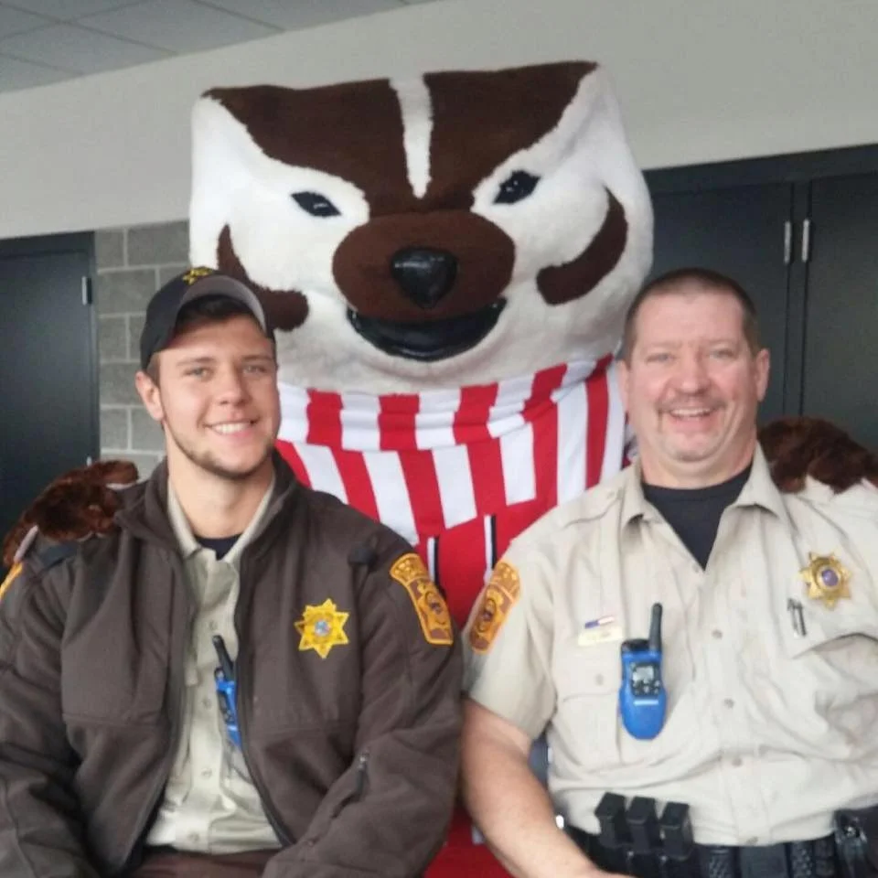 Two men in sheriff uniforms smiling with a large Huskies mascot in the background.