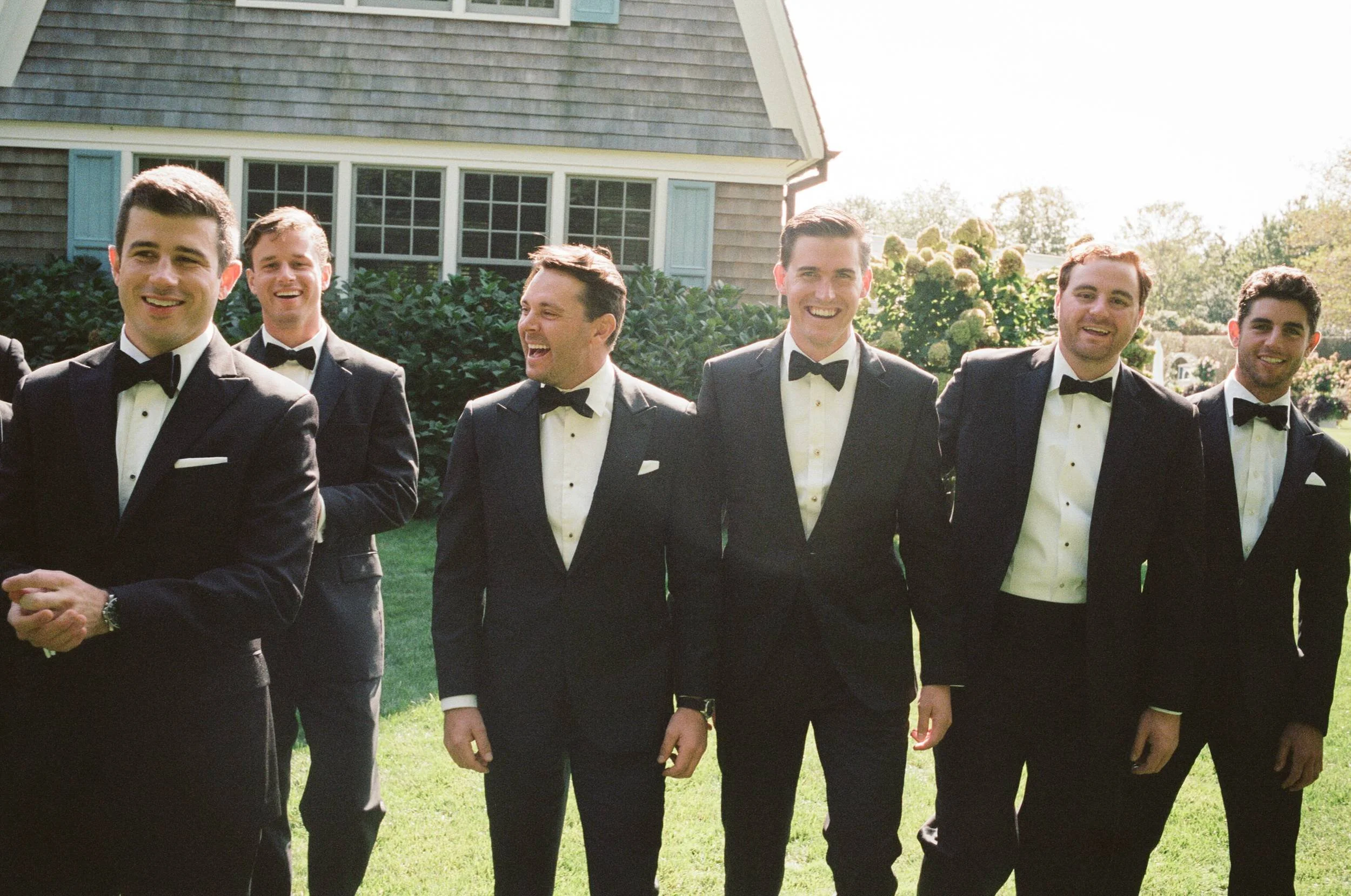 Groom and groomsmen in black tie laughing on the lawn in East Hampton