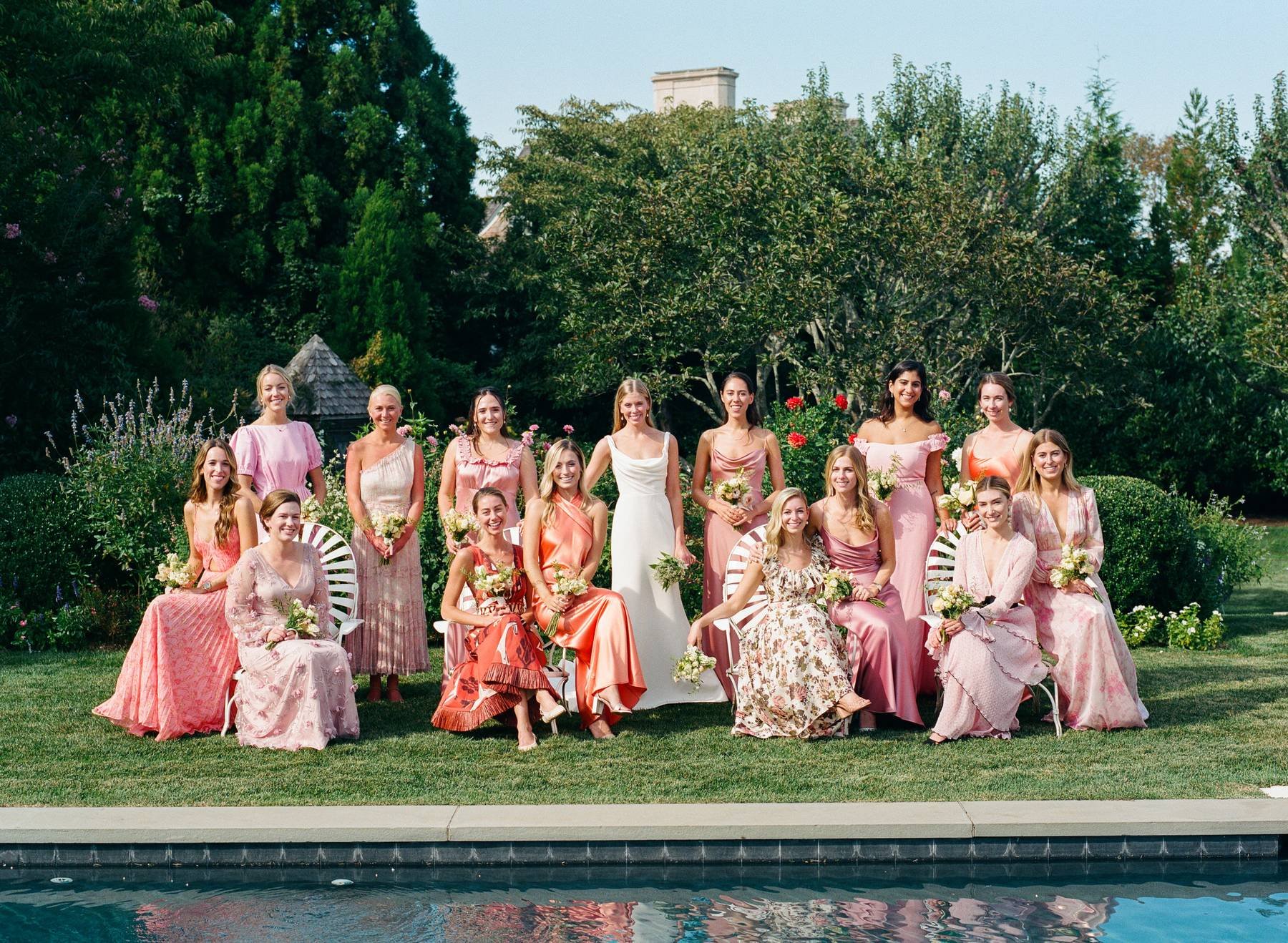 Bridesmaids in pink and coral gathered around the bride by the pool in East Hampton