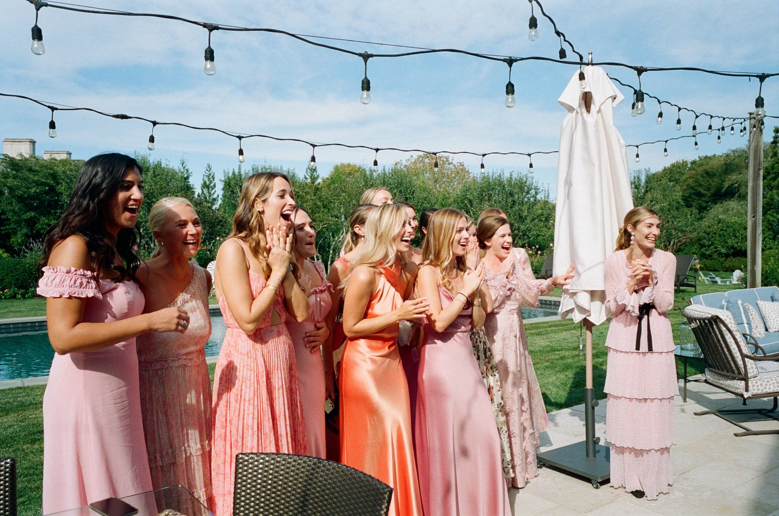 Bridesmaids in pink dresses reacting to seeing the bride by the pool before a Longhouse Reserve wedding in East Hampton