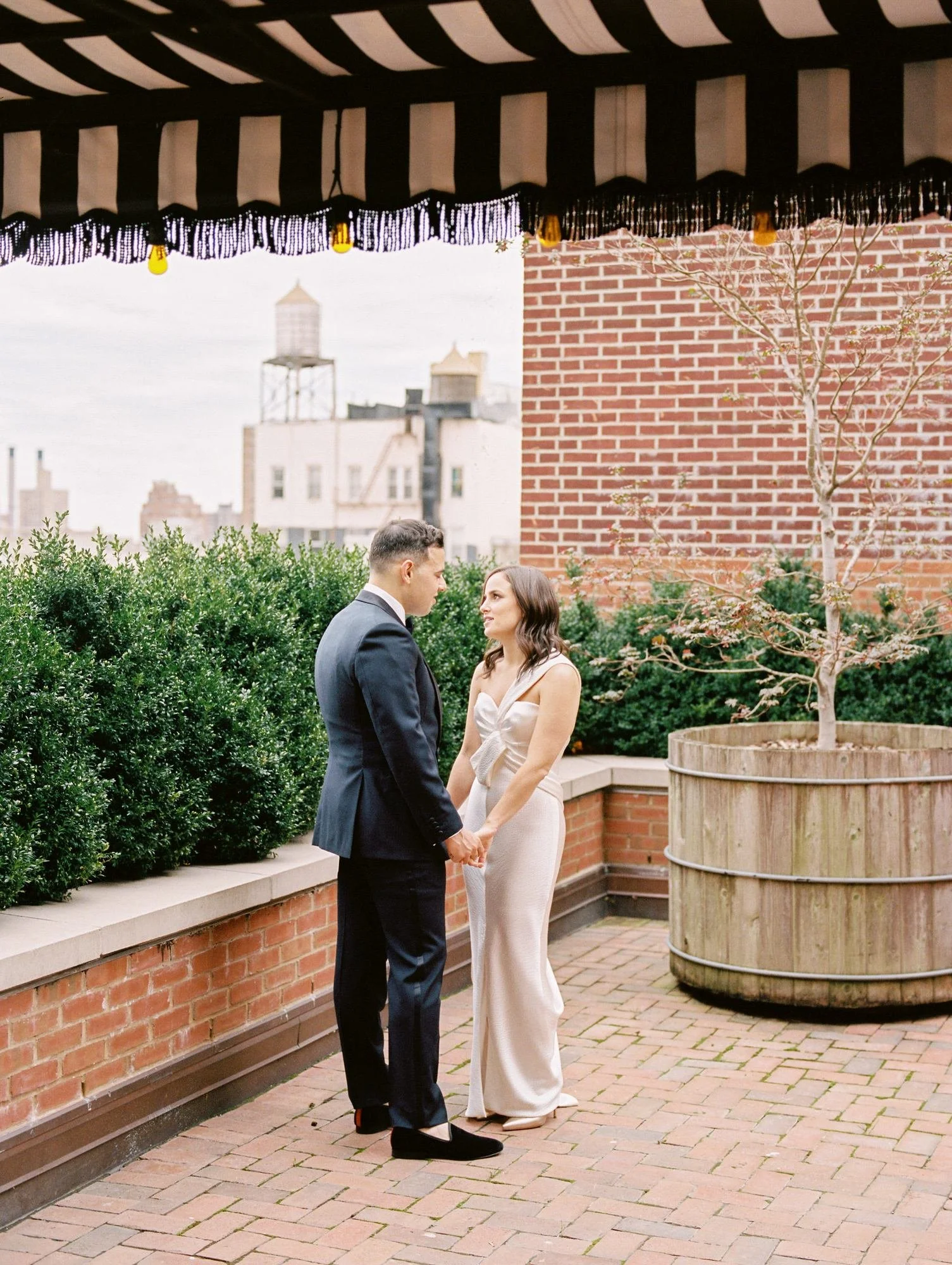 Bride and groom holding hands under the striped awning on The Bowery Hotel terrace