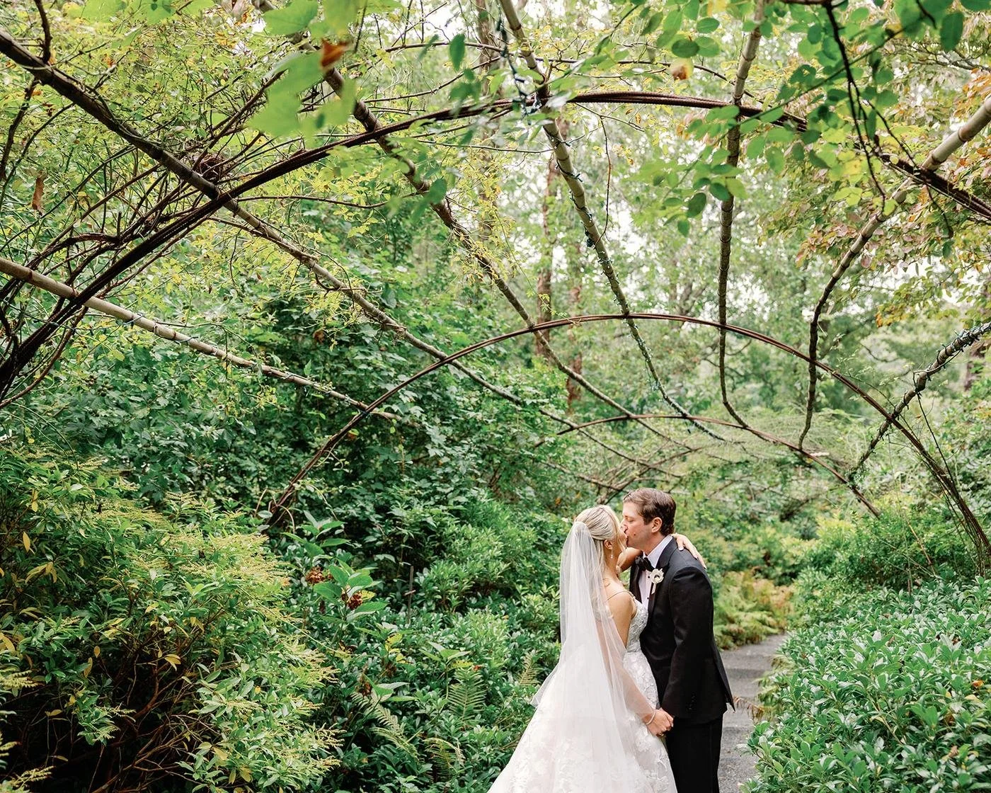 Couple kissing under an arch of branches in the woodland garden at LongHouse Reserve