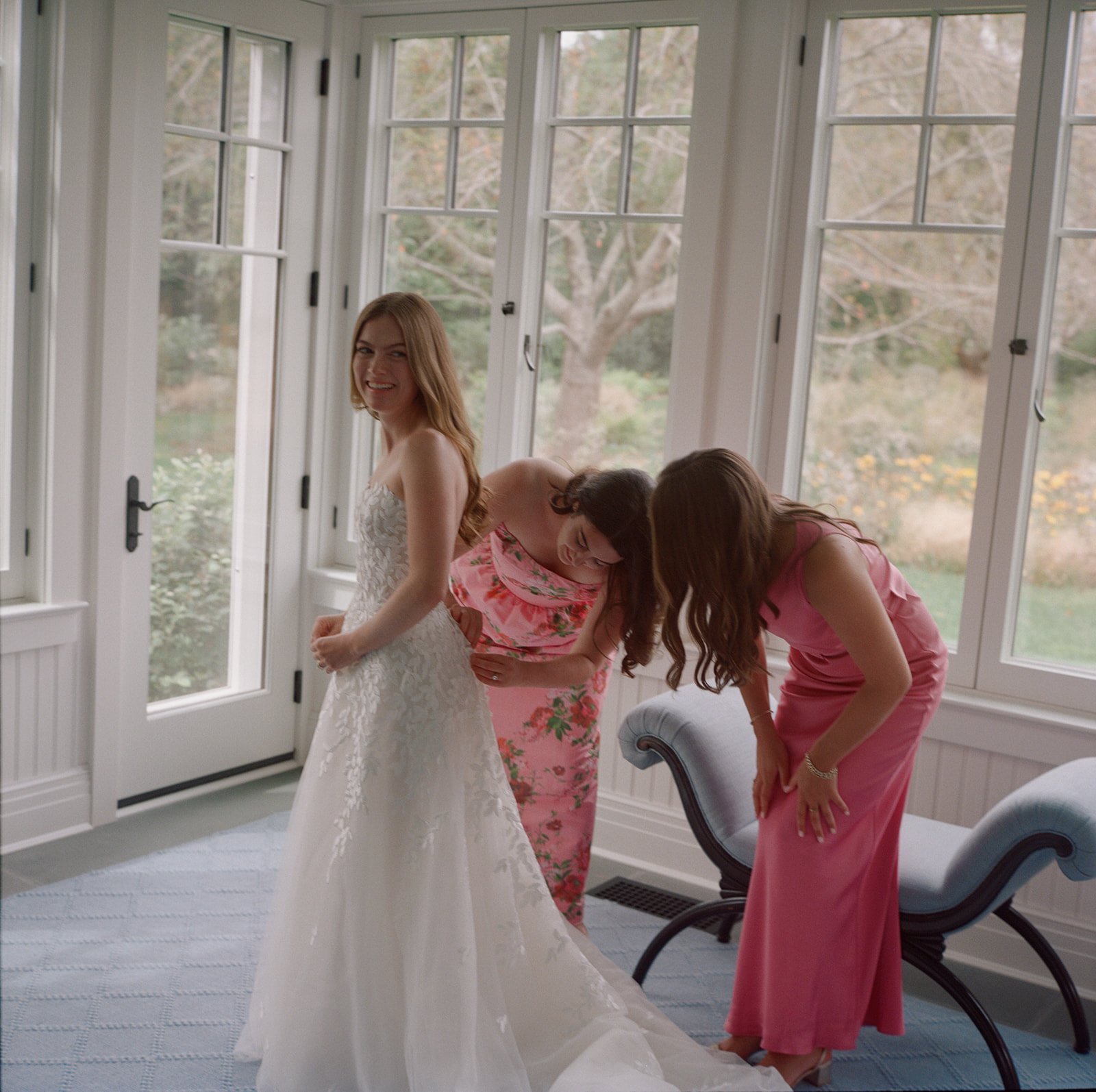 Bridesmaids helping the bride with her dress in a sunroom in East Hampton