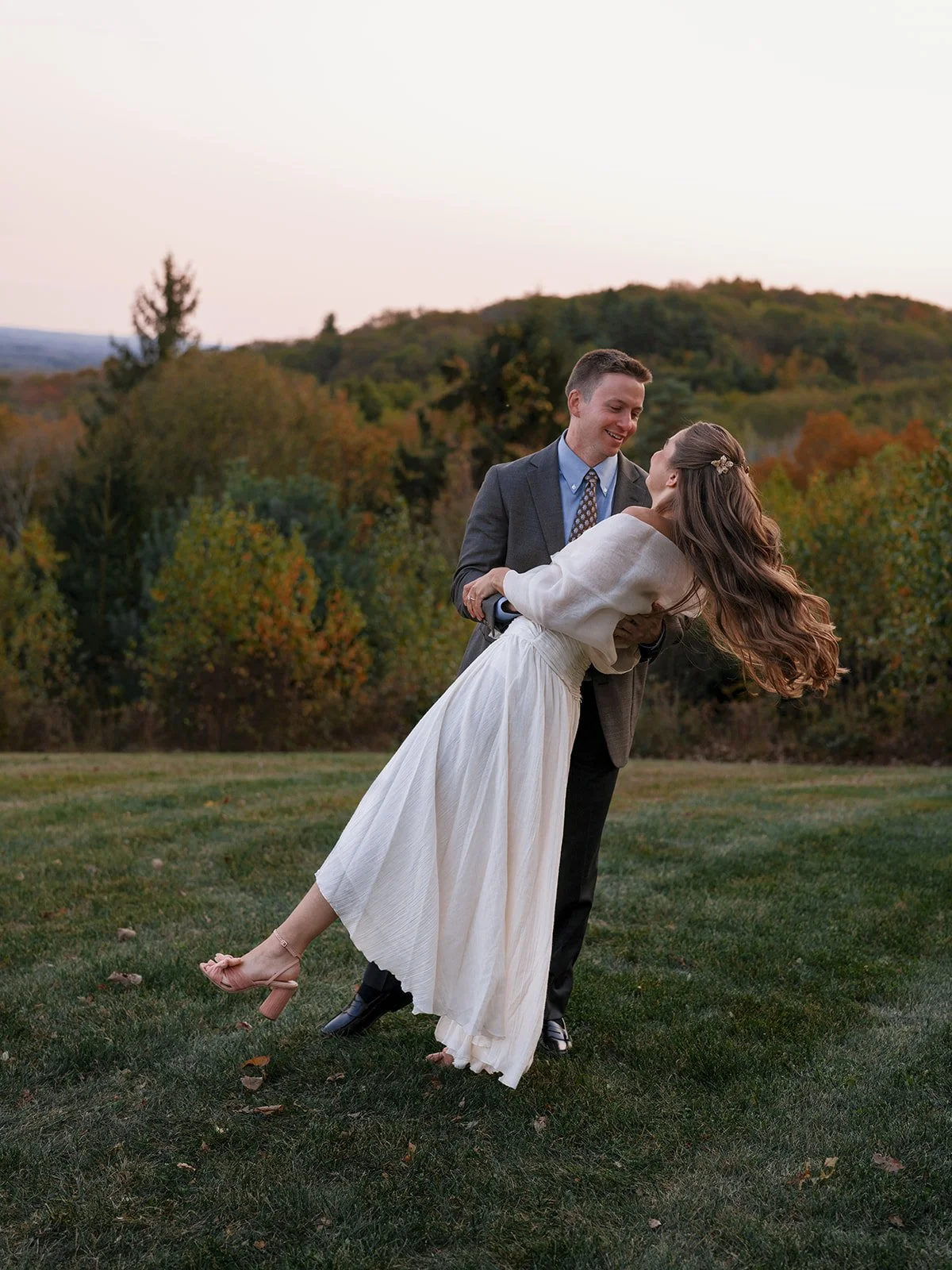 Bride twirling beside the groom on the lawn at dusk during their welcome dinner at Cedar Lakes Estate in Port Jervis, NY
