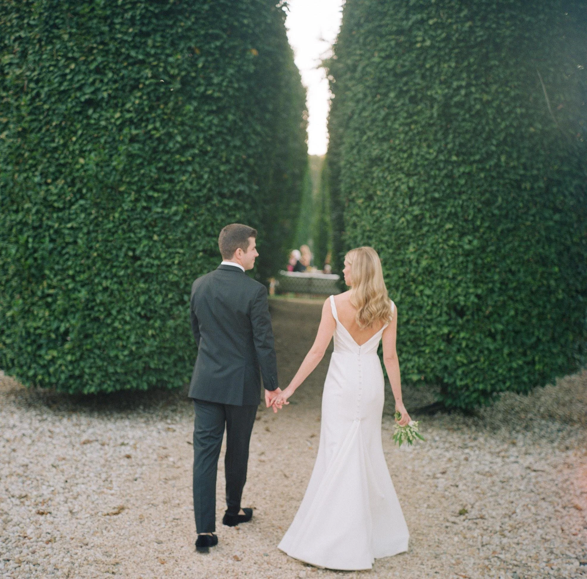 Bride and groom walking hand in hand between tall hedges at LongHouse Reserve, East Hampton