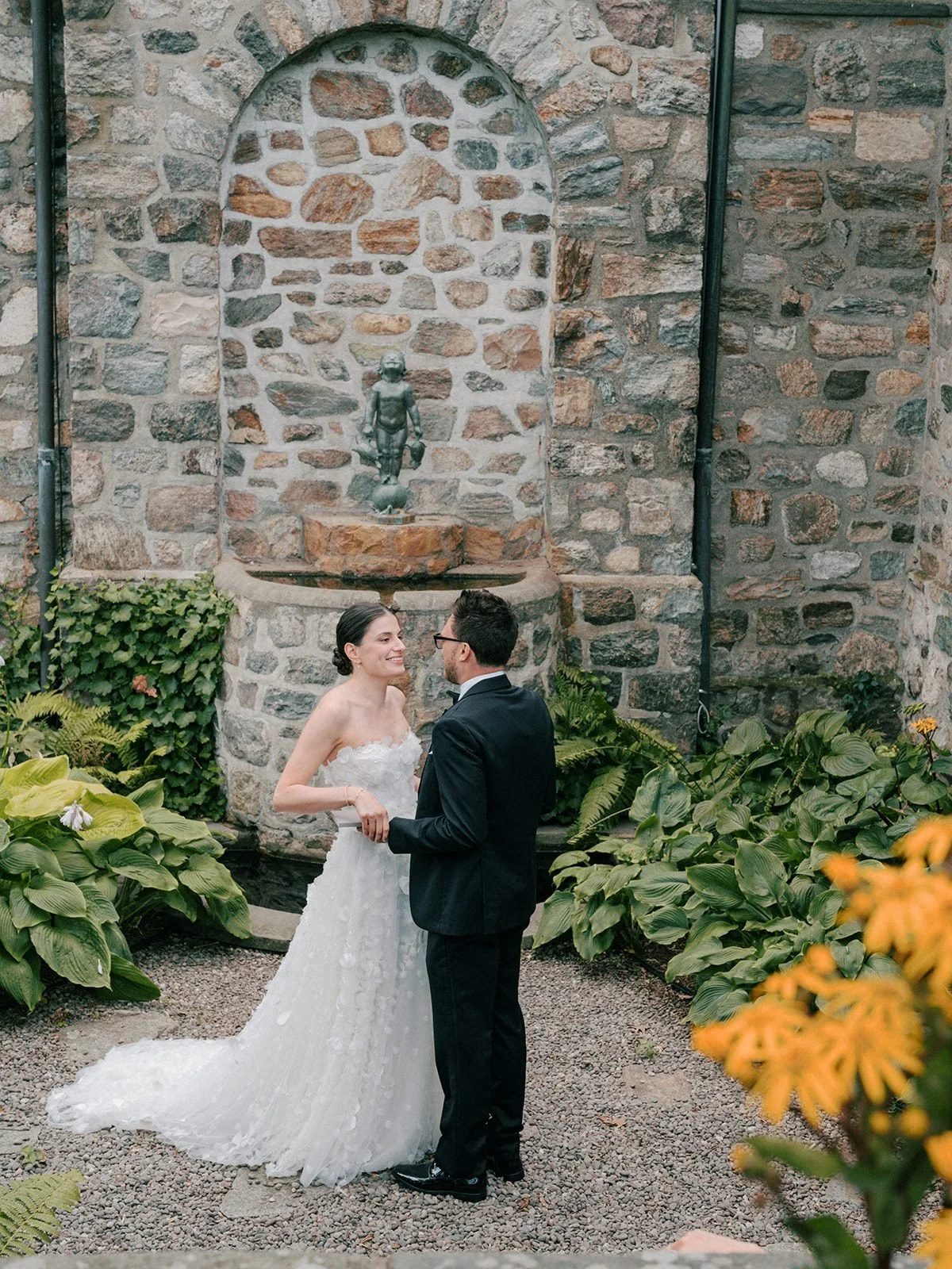 Bride and groom laughing by the stone fountain wall at Glynwood in the Hudson Valley