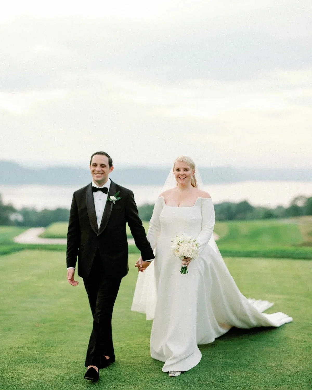 Bride and groom walking across the lawn above the Hudson River at Sleepy Hollow Country Club in Briarcliff Manor, NY