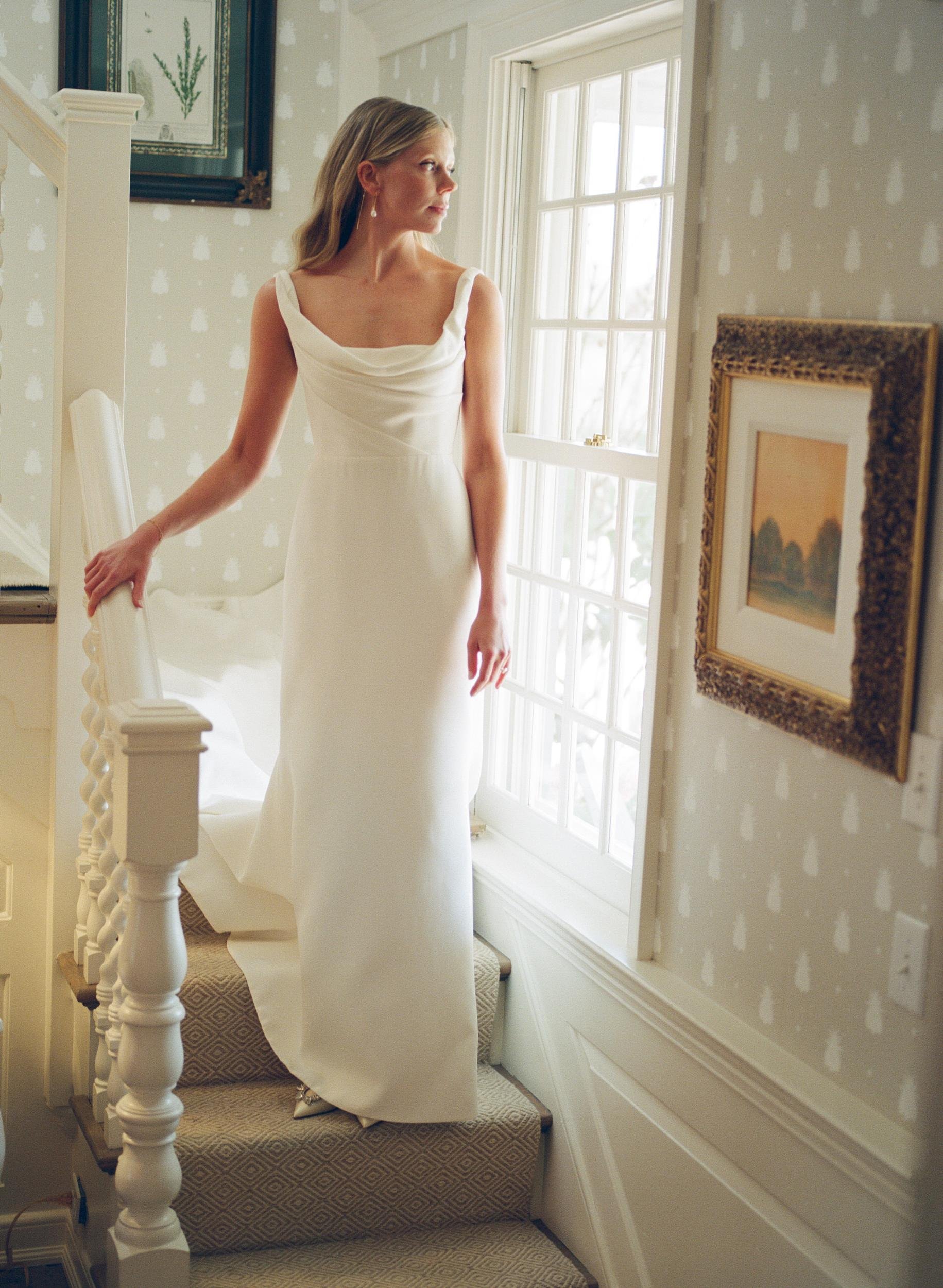 Bride in a fitted gown on the staircase by a sunny window in East Hampton