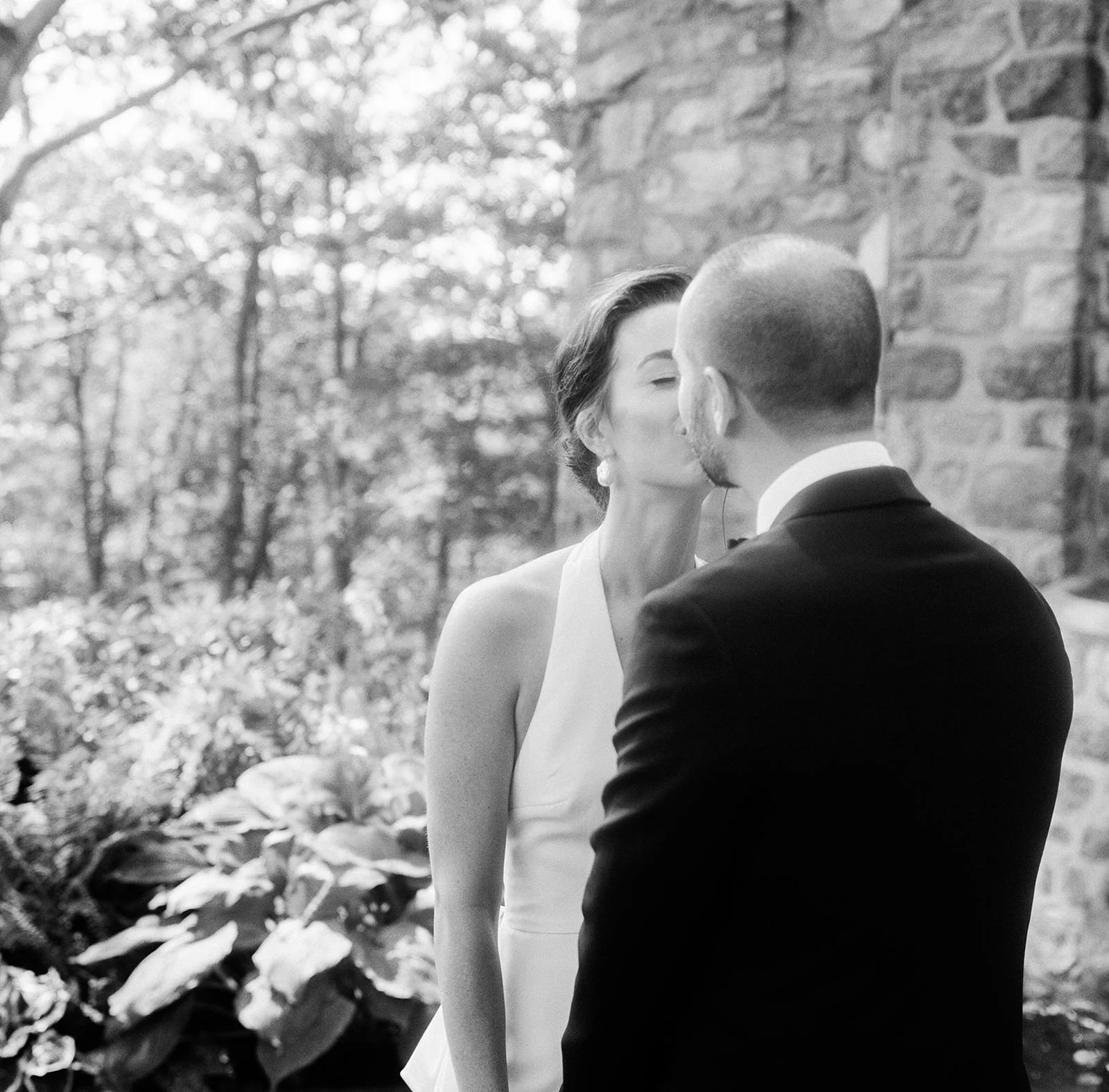 Black and white photo of a couple kissing by the stone wall at Glynwood in Cold Spring