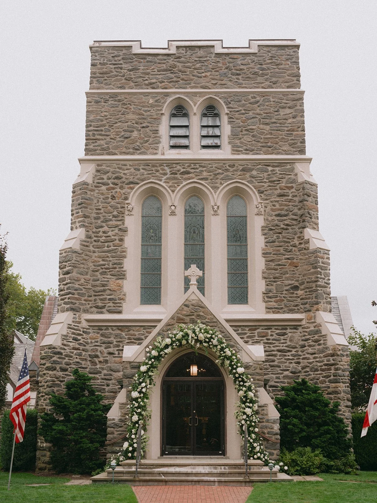 Stone tower of St. Luke's Episcopal Church with a floral arch at the door in East Hampton