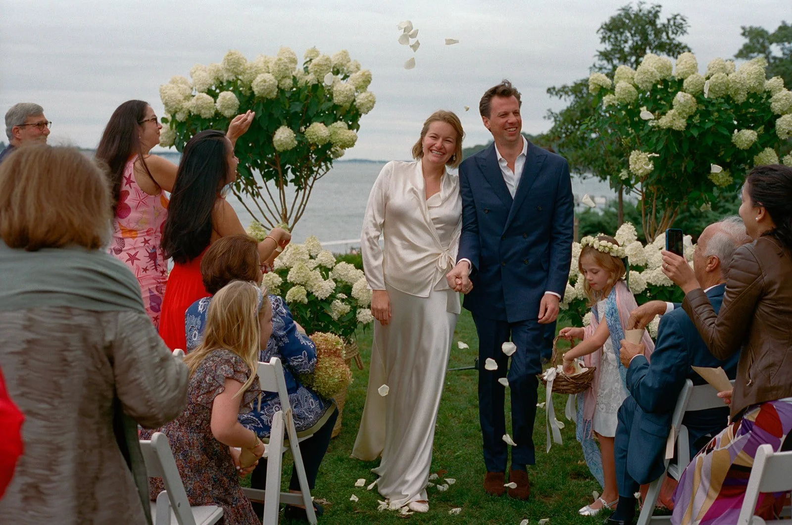 Bride and groom walking up the aisle through flower petals as guests cheer
