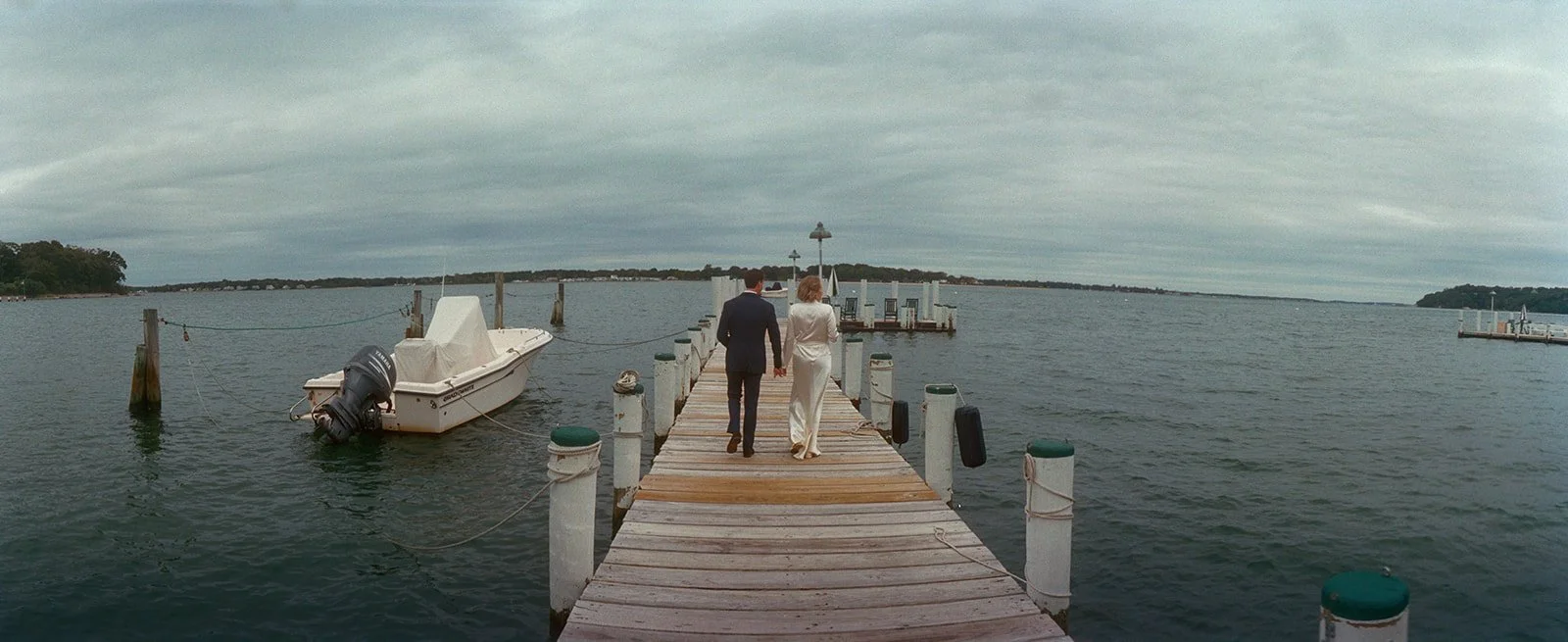 Wide view of the couple walking out on a long dock into the bay on Shelter Island