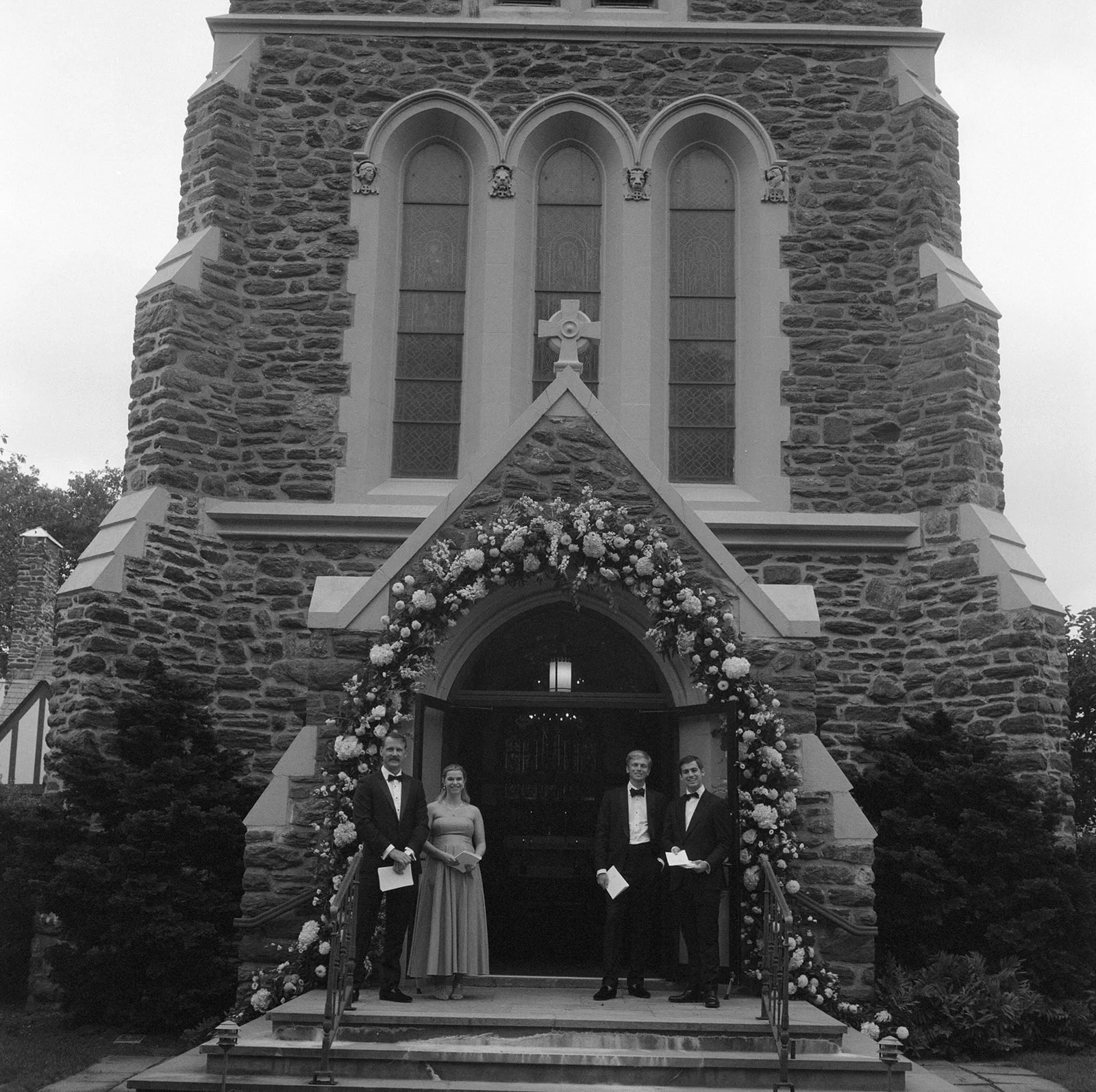Black and white view of the stone front of St. Luke's with the wedding party at the door