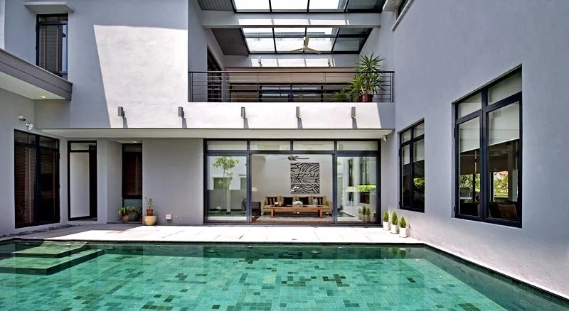 Modern house with a swimming pool in the backyard, outdoor seating area visible through glass doors, and balconies on upper levels.