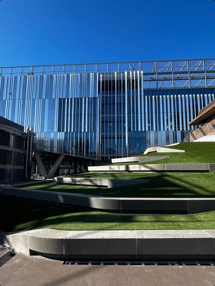 Modern building with glass facade, metal accents, and grass-covered terraces against a clear blue sky.